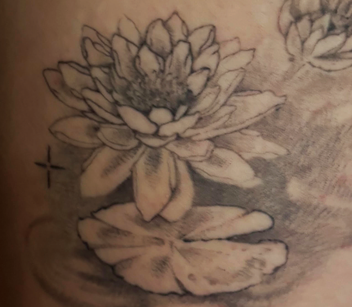 A black and gray tattoo of a flower with leaves.
