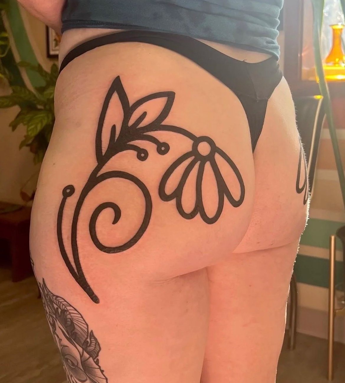 A tattoo of a stylized floral design on a person's upper buttock and hip area, with black ink outlines of leaves and flowers.