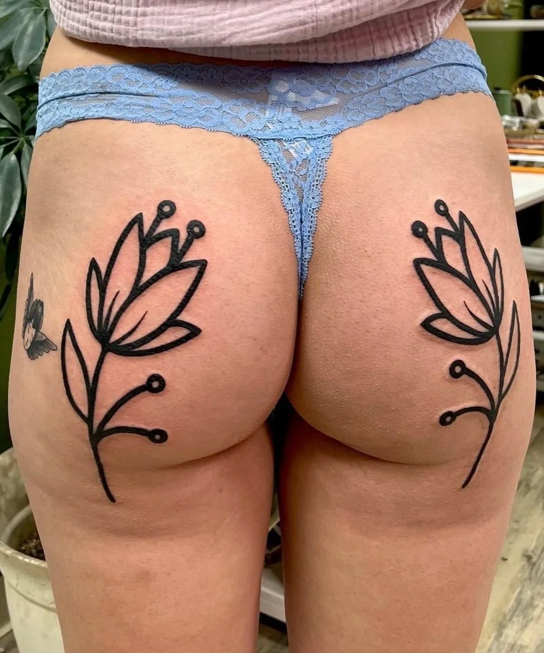 Person wearing blue lace underwear with floral tattoos on both hips.