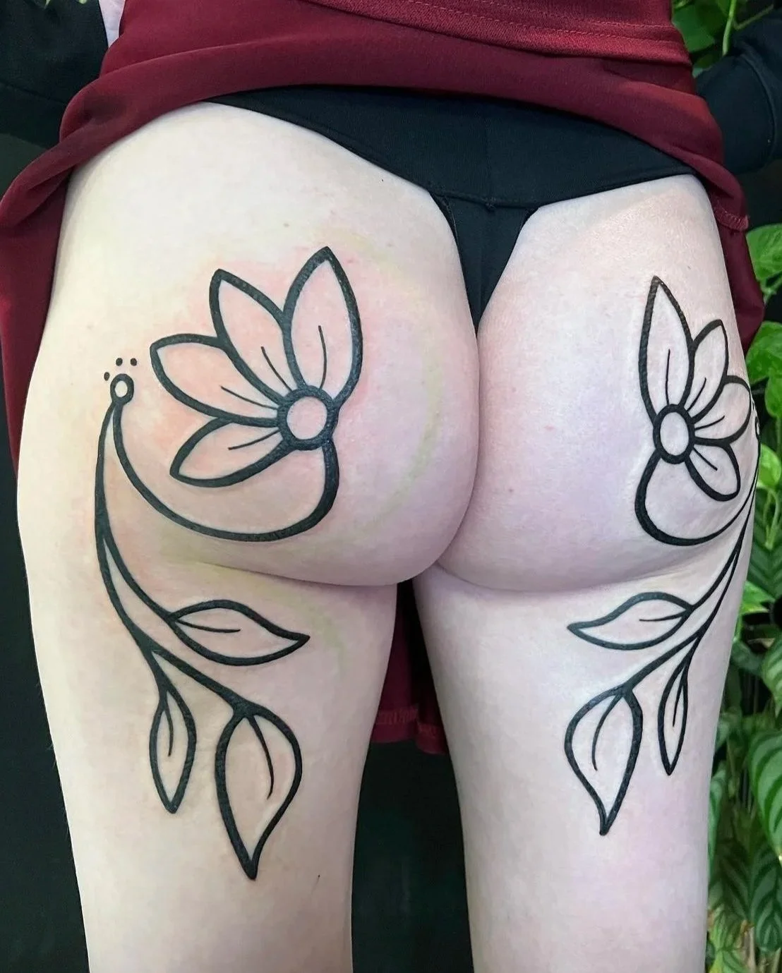 Tattoo of a flower with leaves on each thigh.