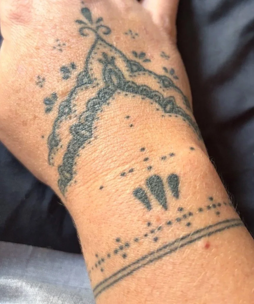 Close-up of a wrist tattoo with a cloud or floral design, dots, and lines.