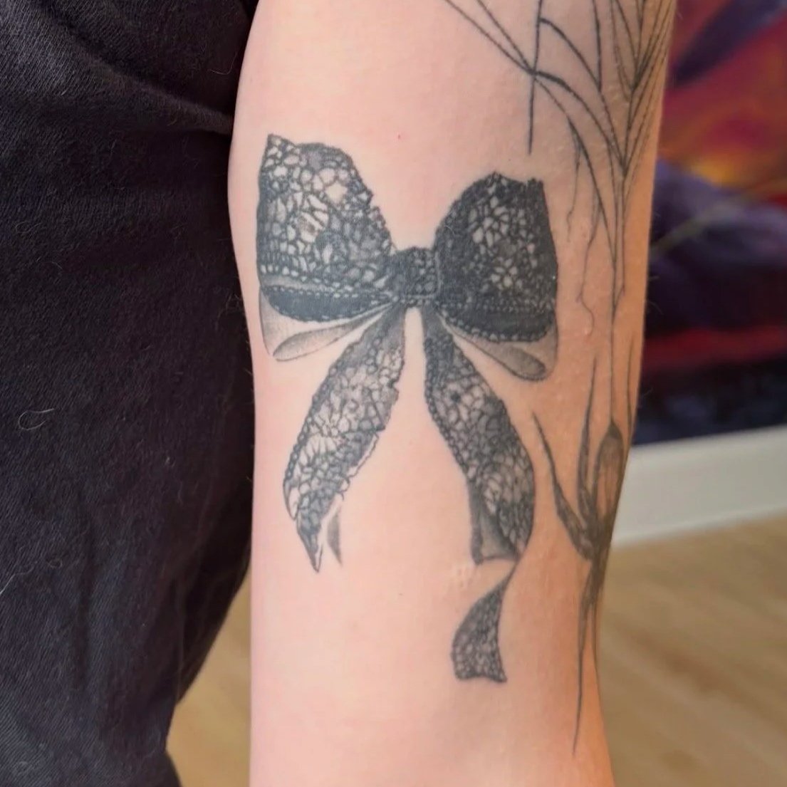 Tattoo of a butterfly on someone's arm, depicted with lace-like intricate patterns in black ink.