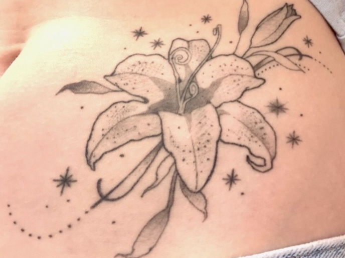 Tattoo of a lily flower with stars and dotted accents on skin.
