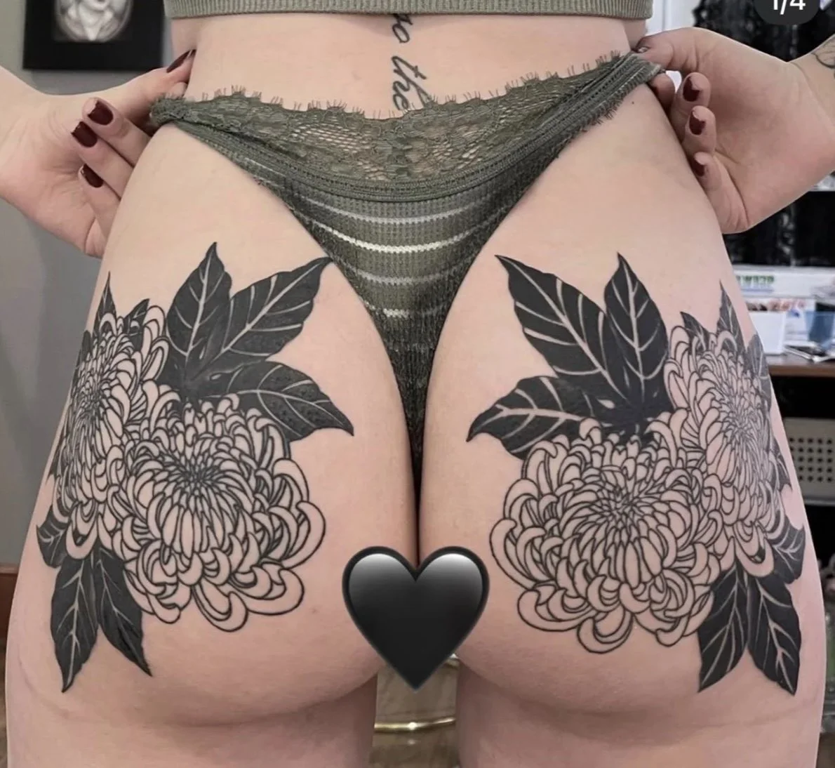 Tattooed floral design on upper thighs with large leaves and intricate blooming flowers, partially visible with a black heart covering the genital area, worn with lace underwear.