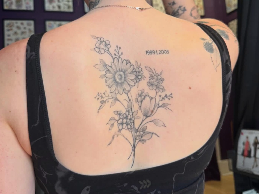 Black and gray floral tattoo on upper back with the dates 1999 and 2003.