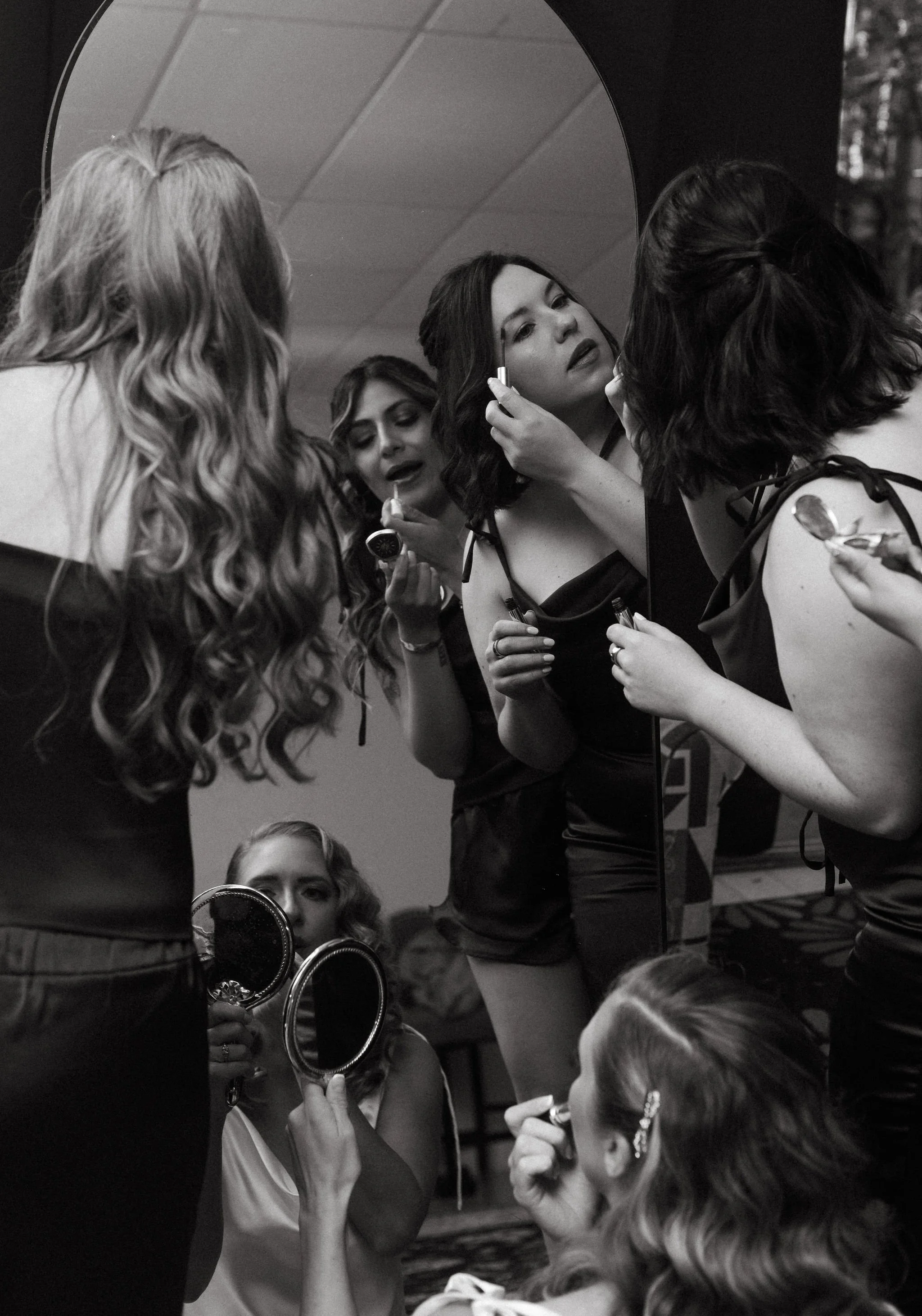 Group of women applying makeup in front of a mirror at a dressing room