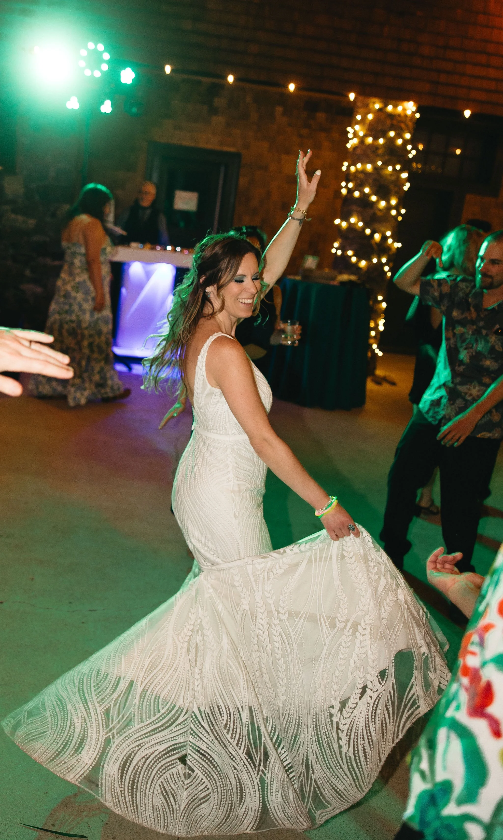 A woman dancing at a celebration, wearing a white dress, with a decorated Christmas tree and other guests in the background.