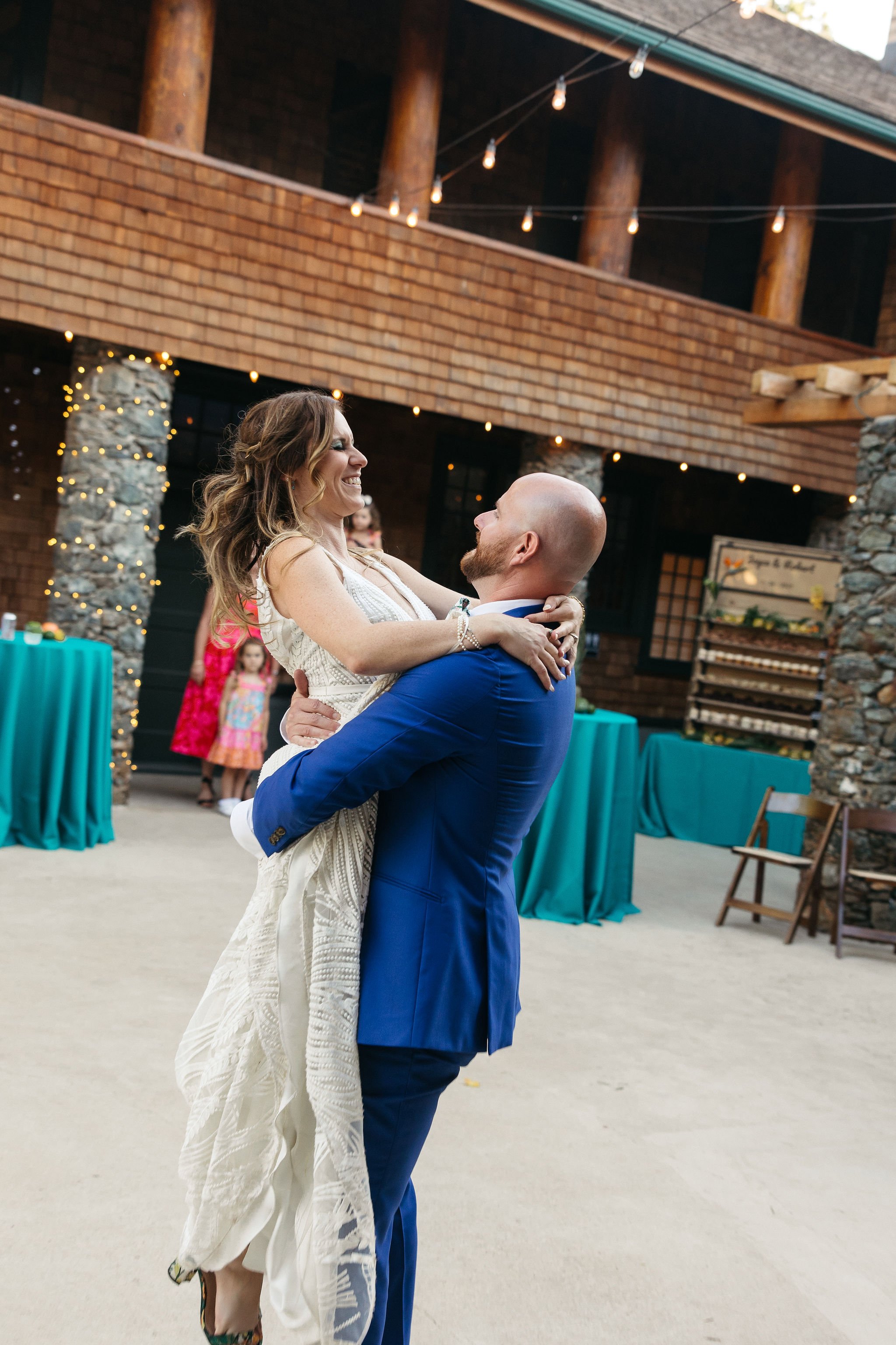 A couple dancing at a wedding reception indoors, with string lights overhead and decorated tables in the background.