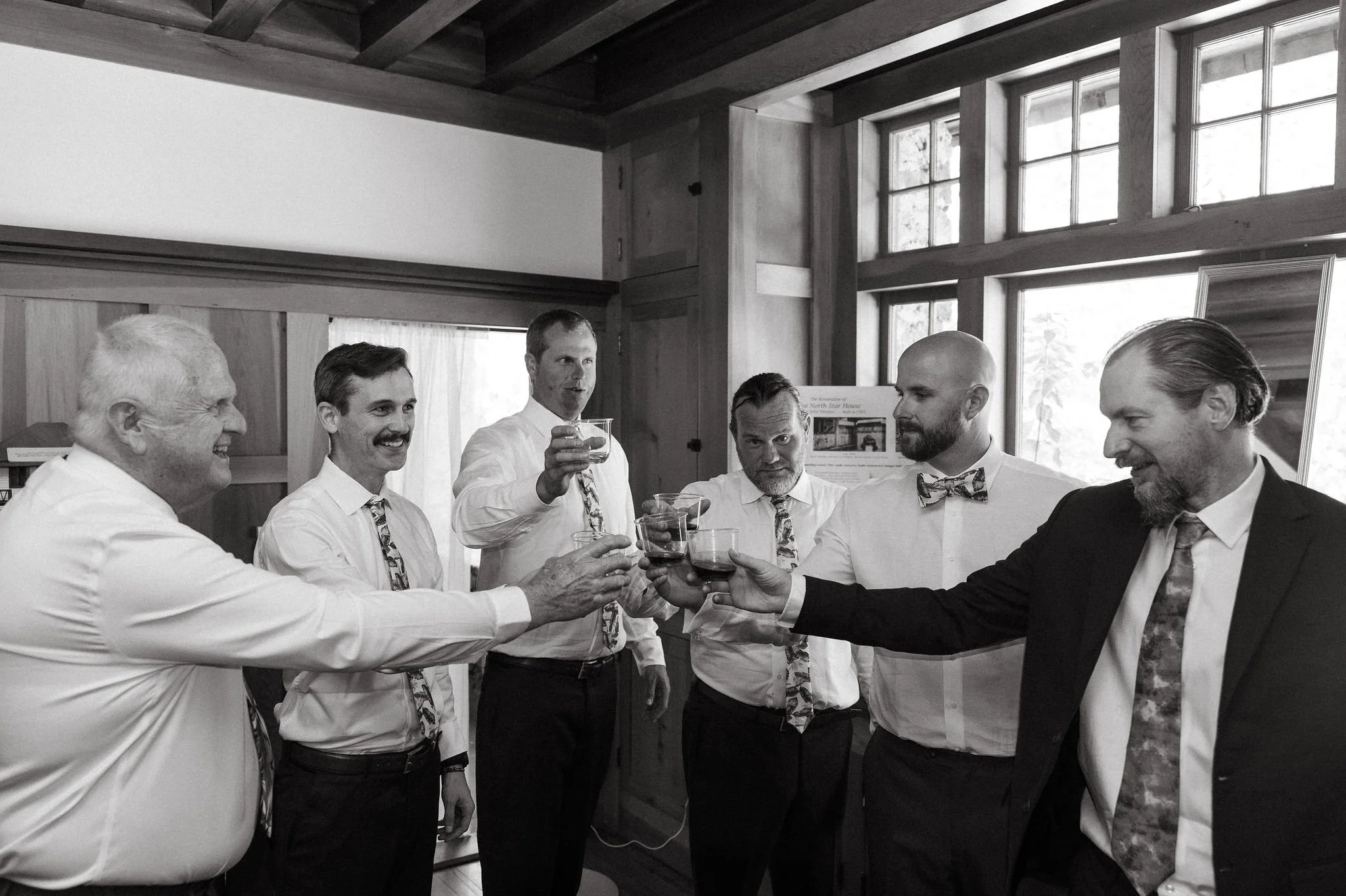 Group of men in formal attire having drinks, raising glasses for a toast in a wooden-paneled room with large windows.
