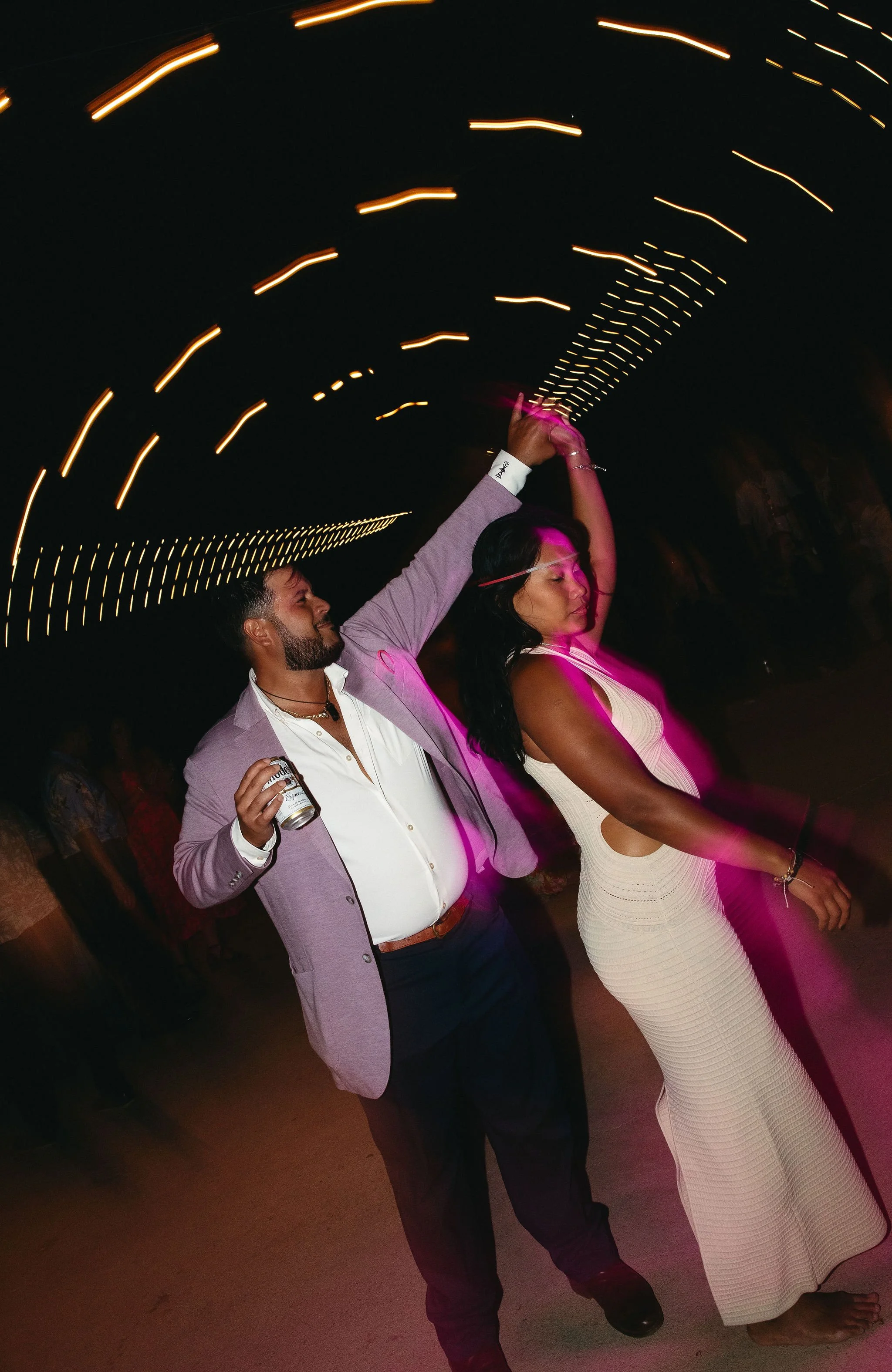 A man and woman dancing together at a party or celebration, with colorful lights and motion blur creating a festive atmosphere.