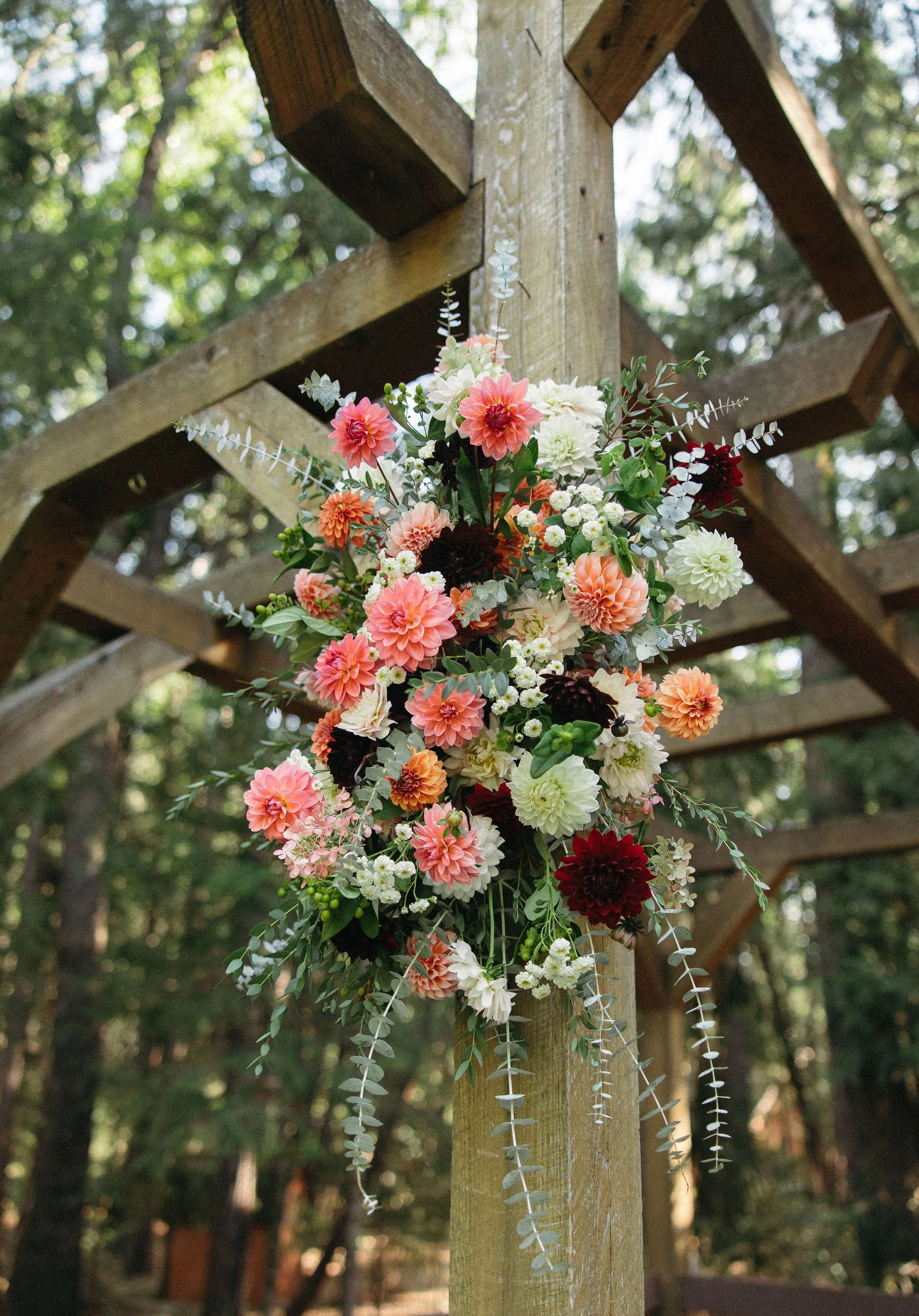 A bouquet of assorted colorful flowers attached to a wooden post outdoors with trees in the background.