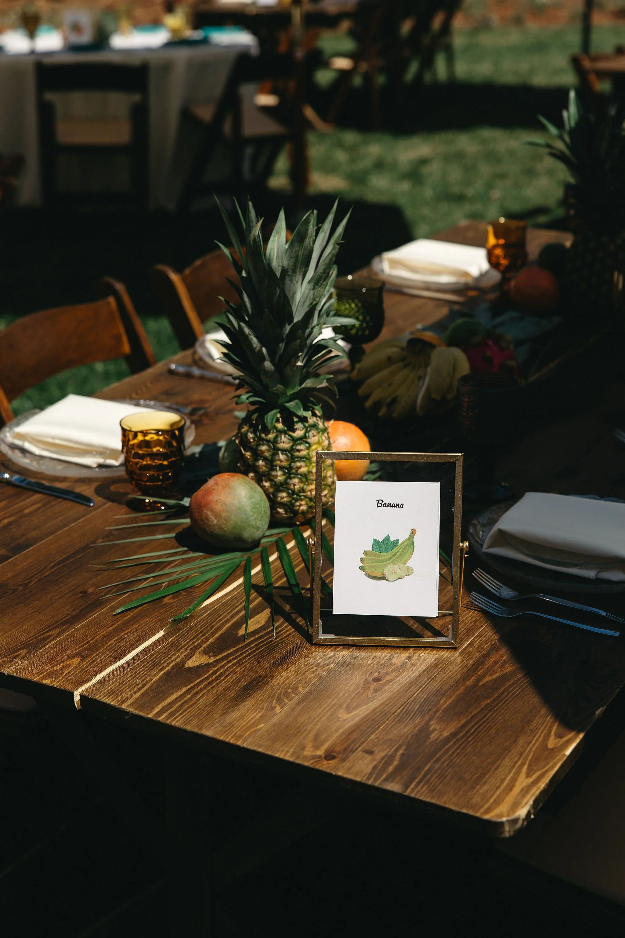 Table decorated with pineapple, bananas, and tropical greenery, with a sign labeled 'Banana' on a framed stand.