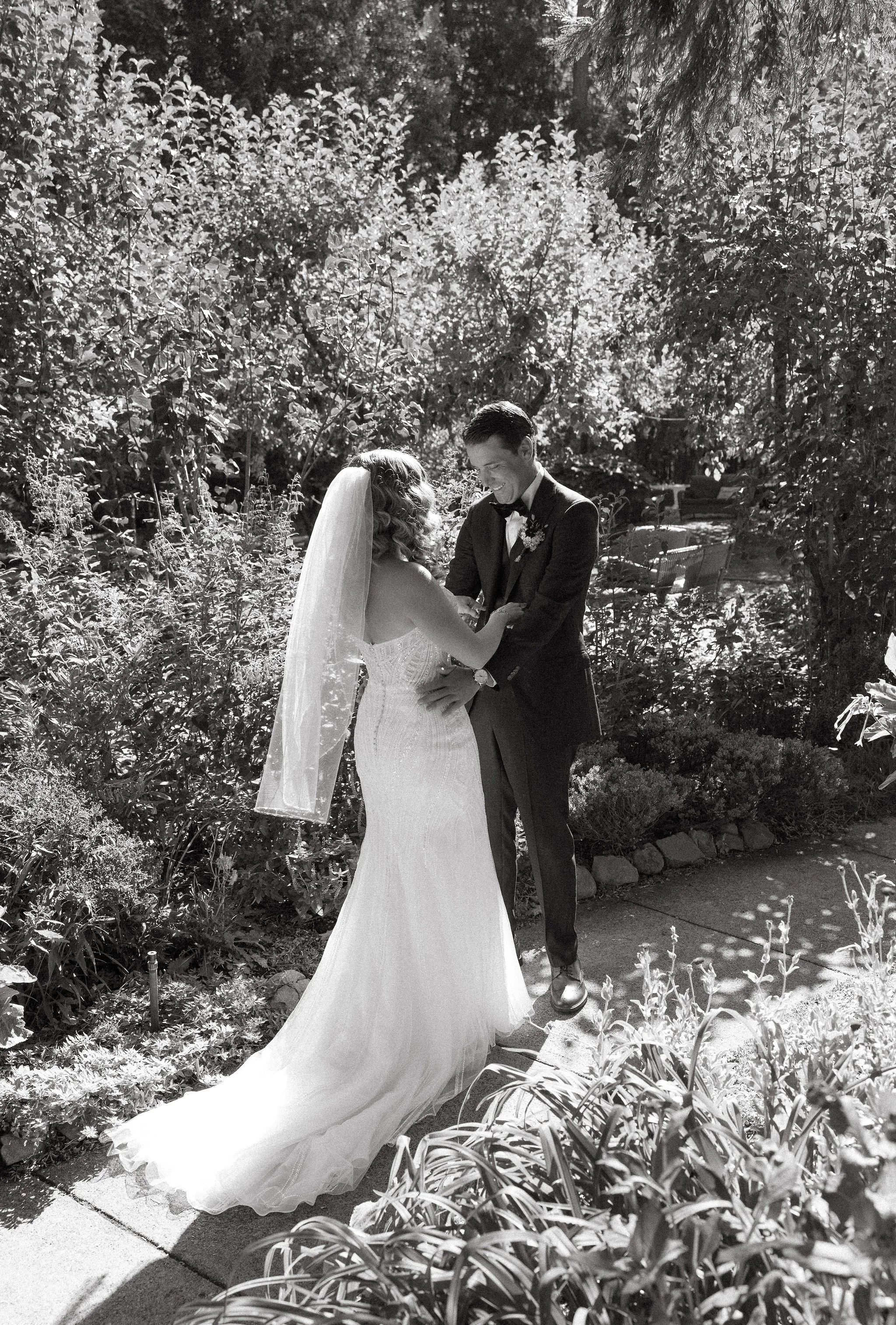 Black and white photo of a bride and groom dancing outdoors surrounded by plants and trees.
