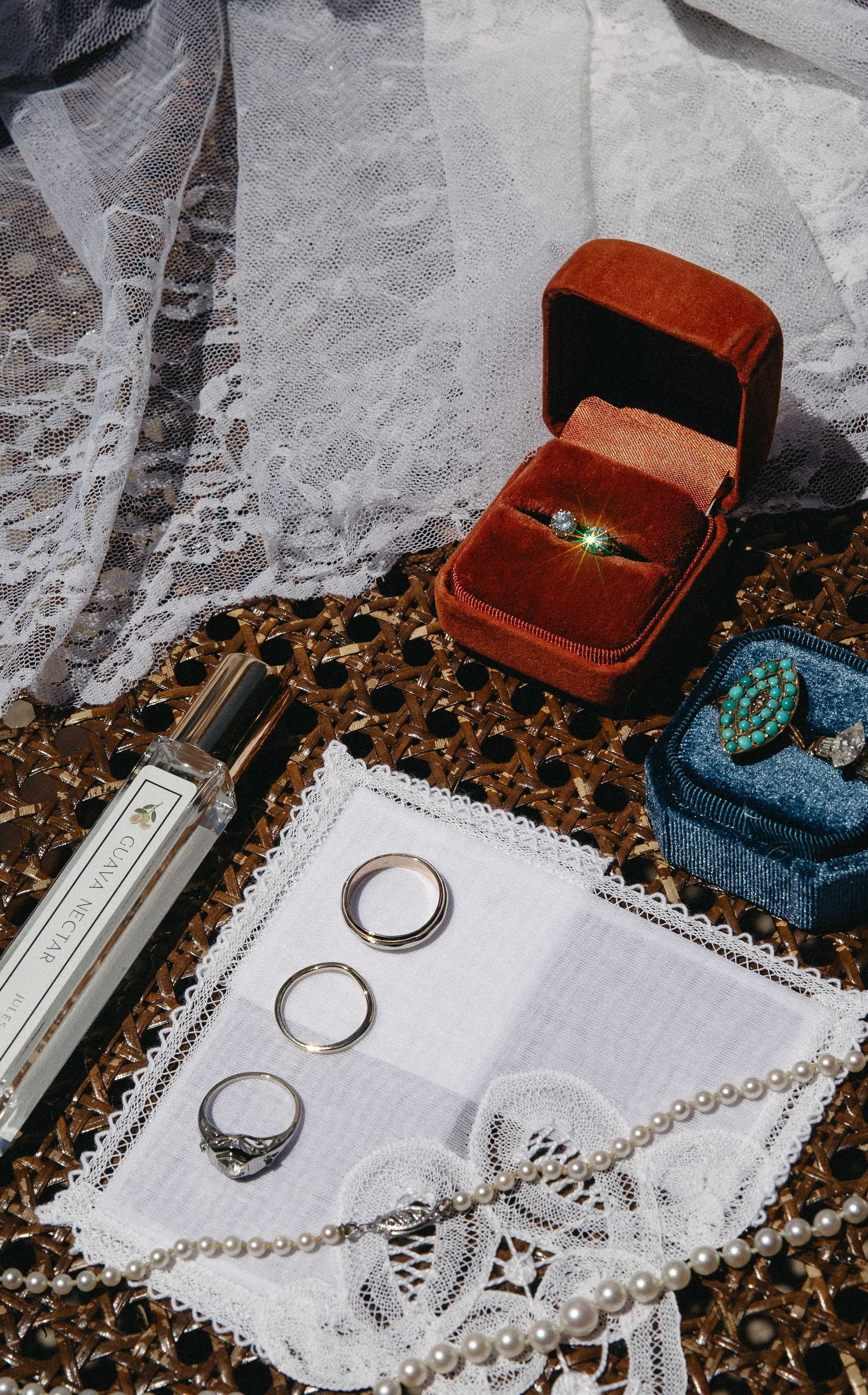 A collection of jewelry and accessories, including rings, a pearl necklace, a turquoise and gold brooch, an engagement ring, a perfume bottle, and a velvet jewelry box with a diamond ring, arranged on a lace cloth.