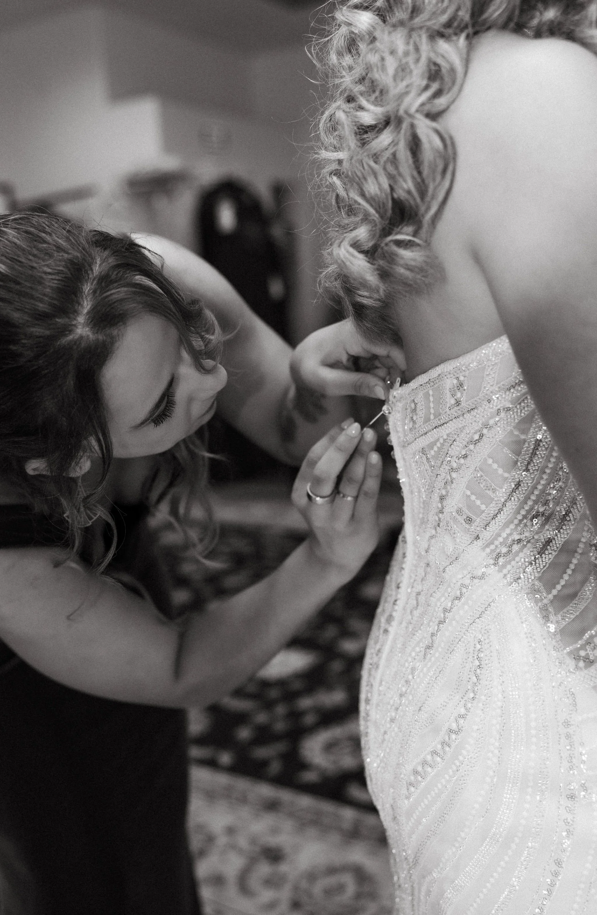 A woman helping a bride with her wedding dress as she pins her dress near the shoulder in preparation for her wedding.