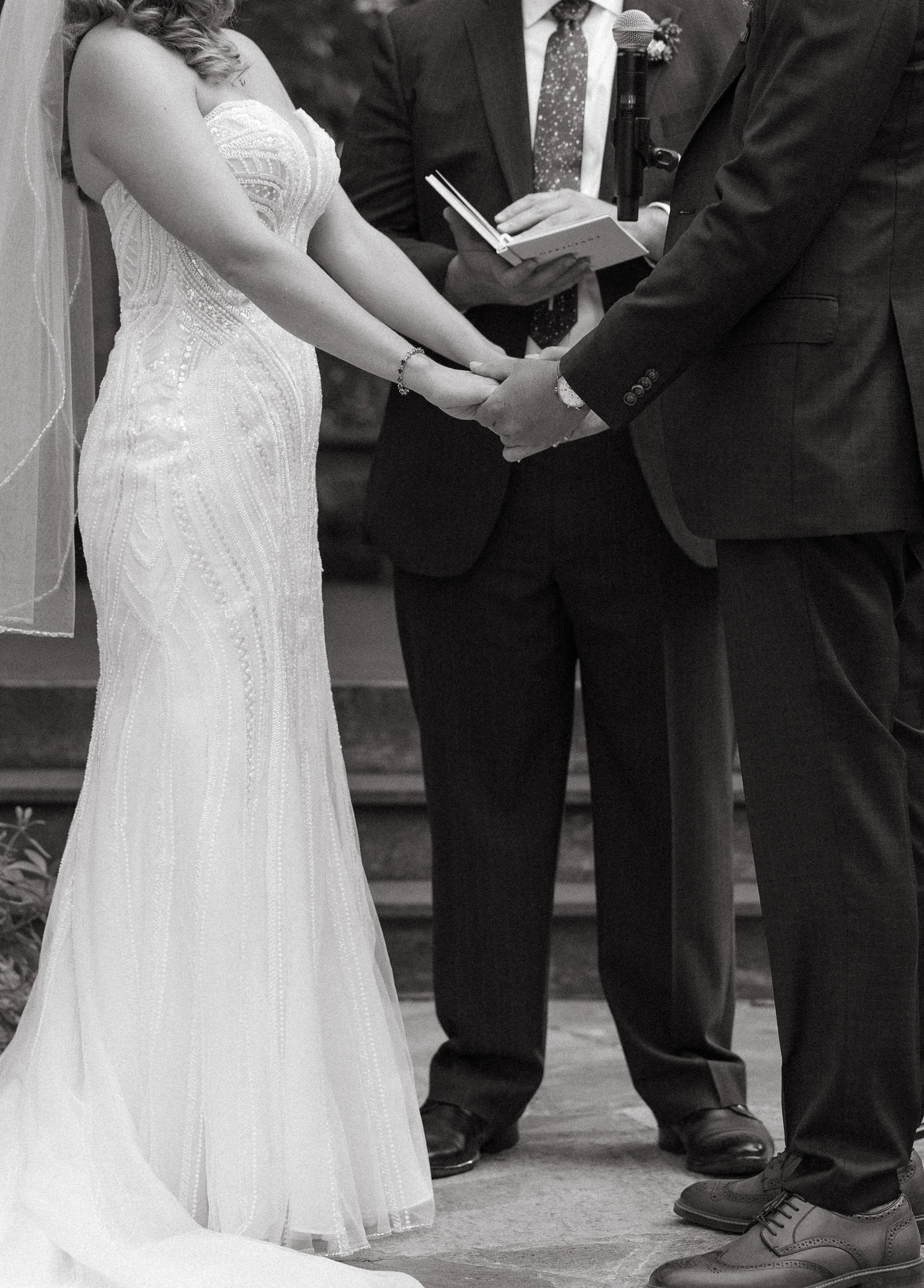 A bride and groom holding hands during their wedding ceremony, with an officiant present.