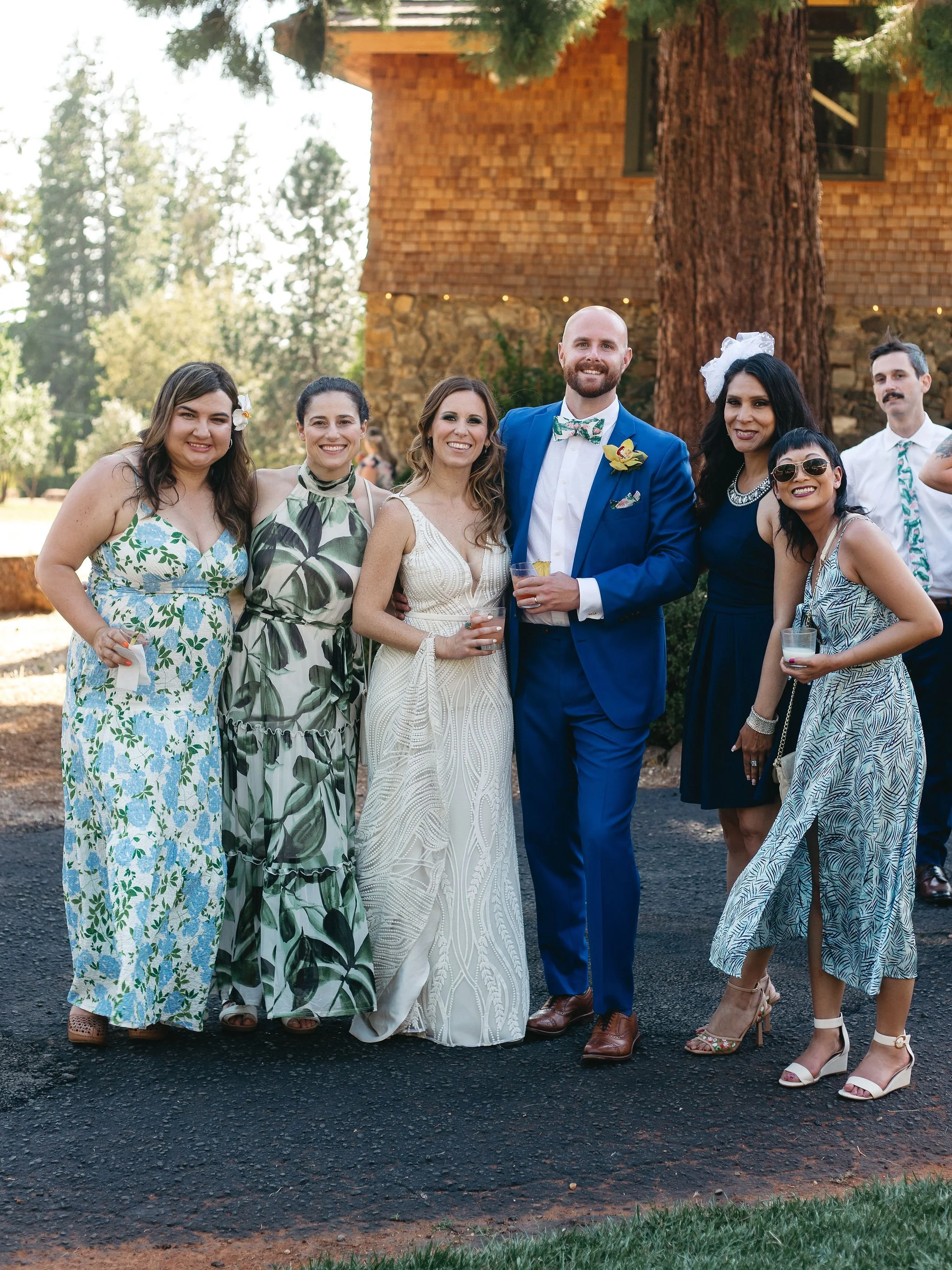 Group of people dressed in formal and summer attire, posing outdoors at a wedding celebration.