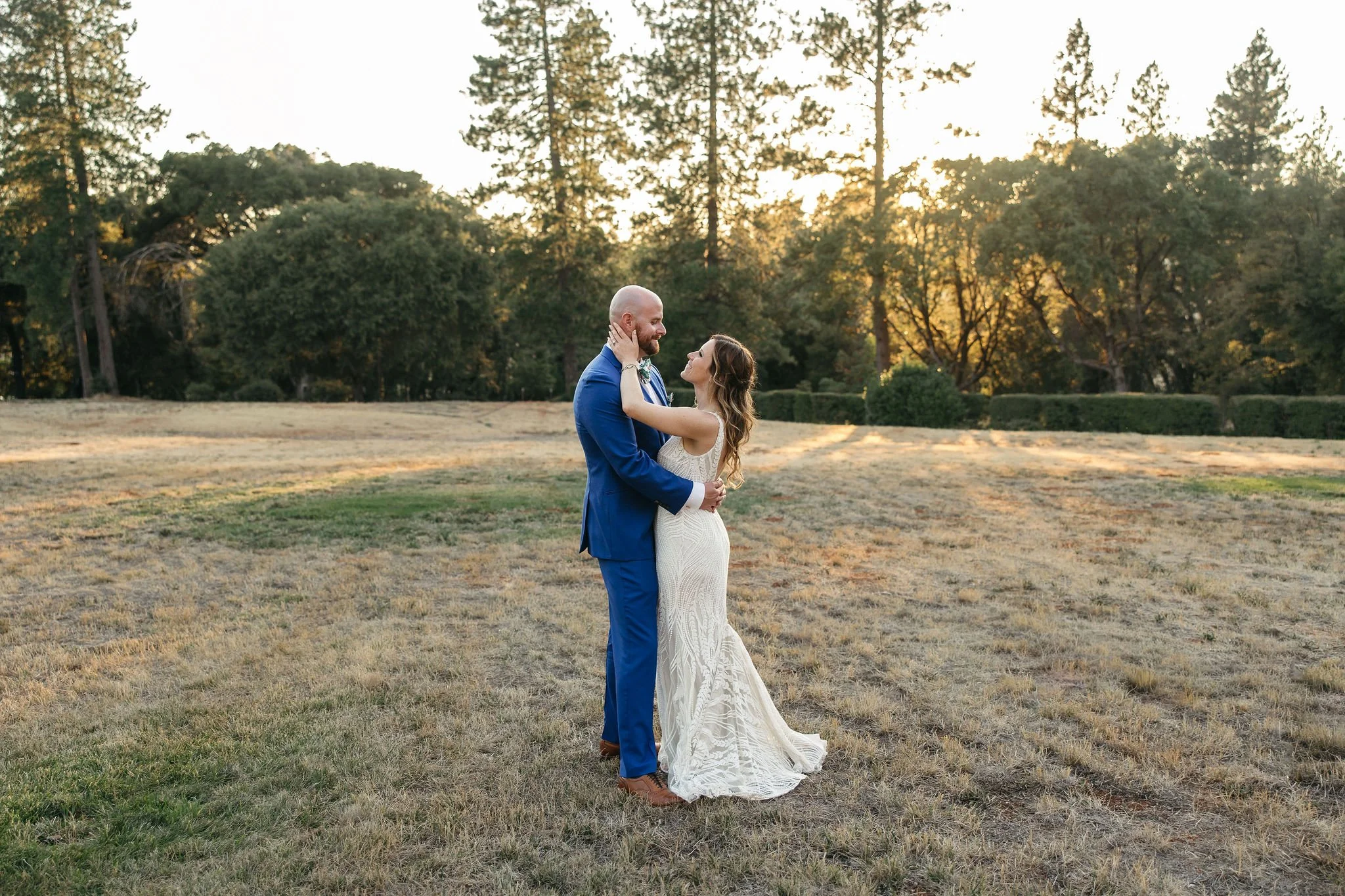 A bride and groom dancing outdoors during sunset in a grassy field with trees in the background.