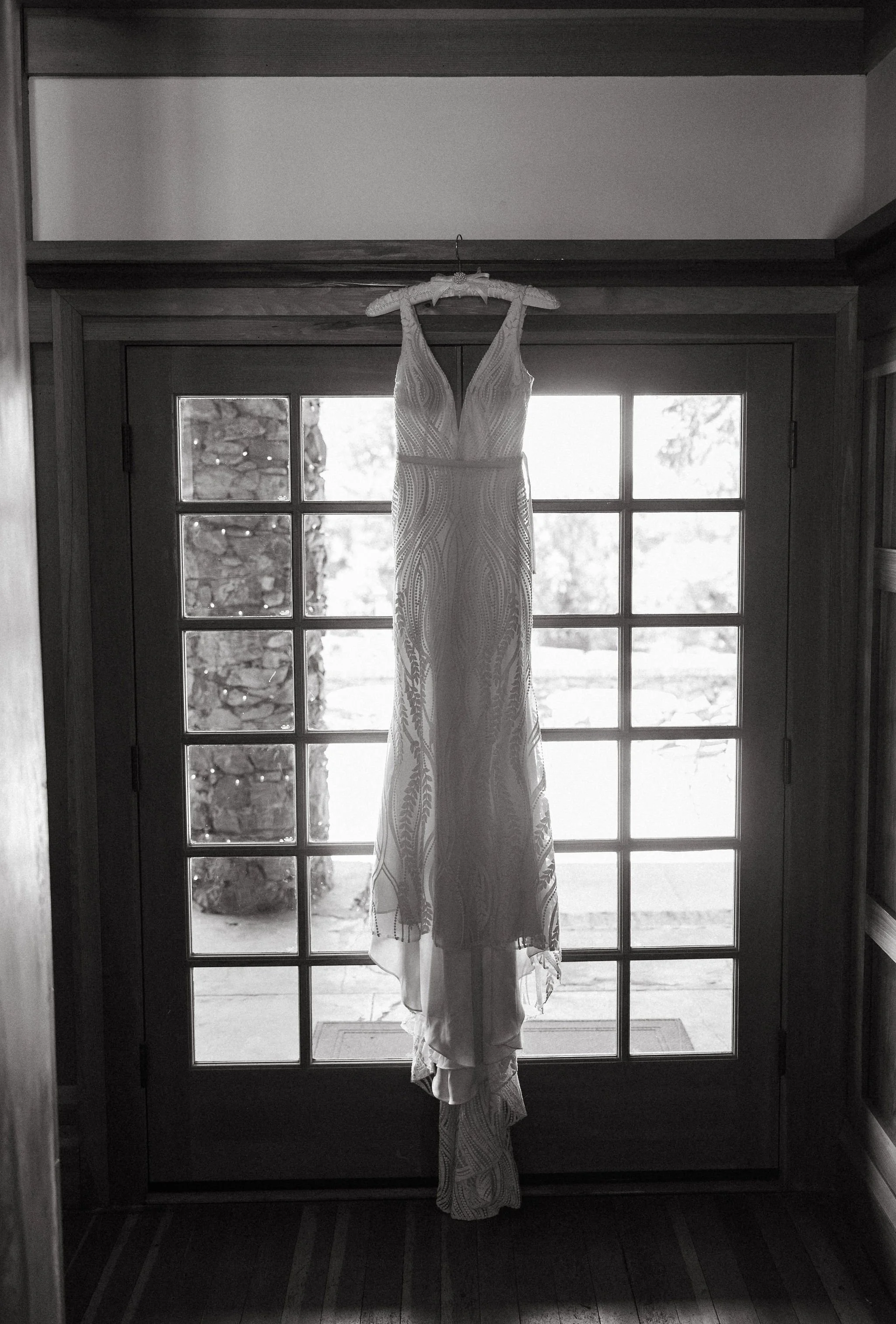 A wedding dress hanging on a hanger in front of a glass door with a palm tree outside.