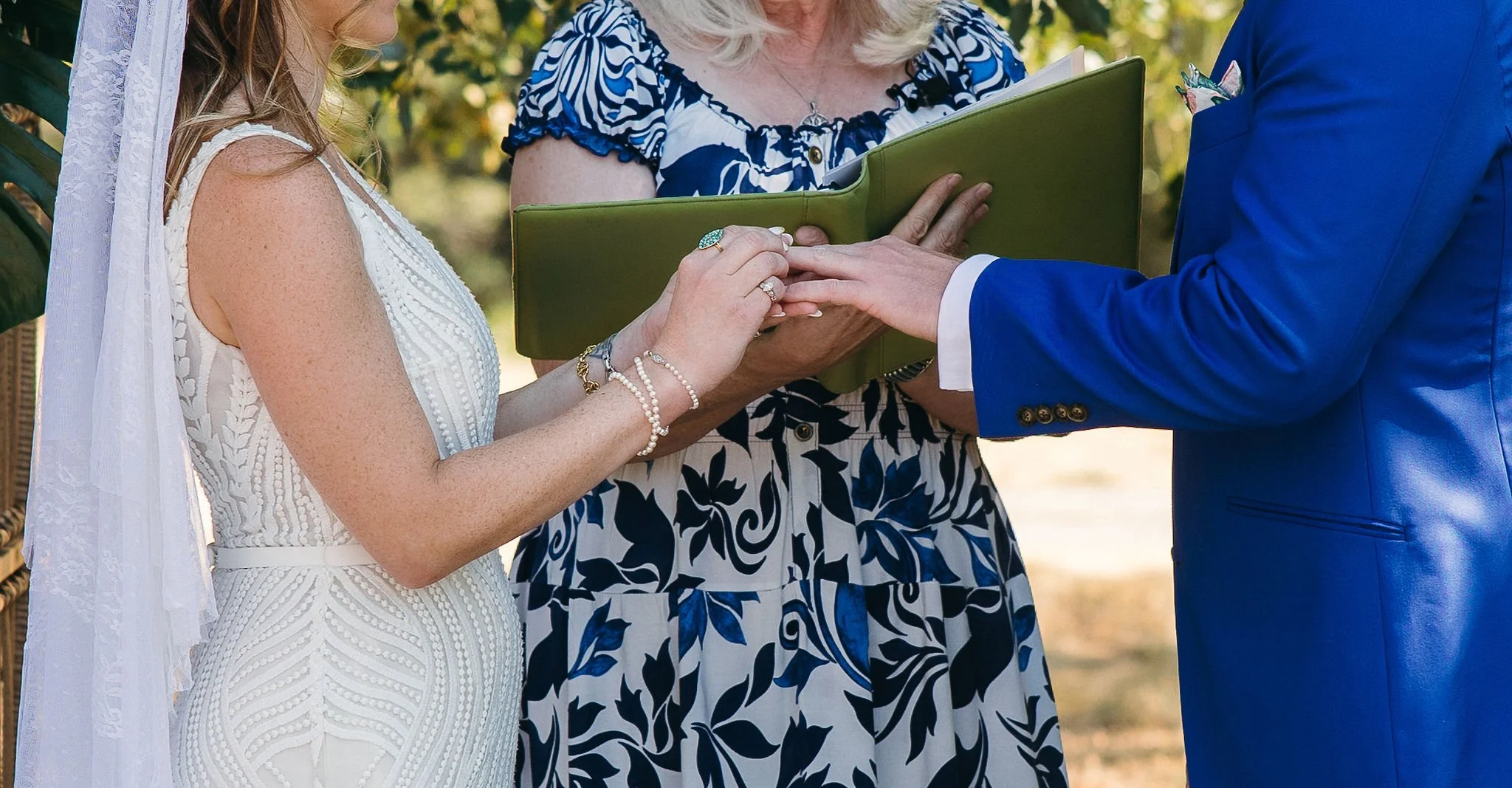 A woman in a white wedding dress and a man in a blue suit holding hands during a wedding ceremony.