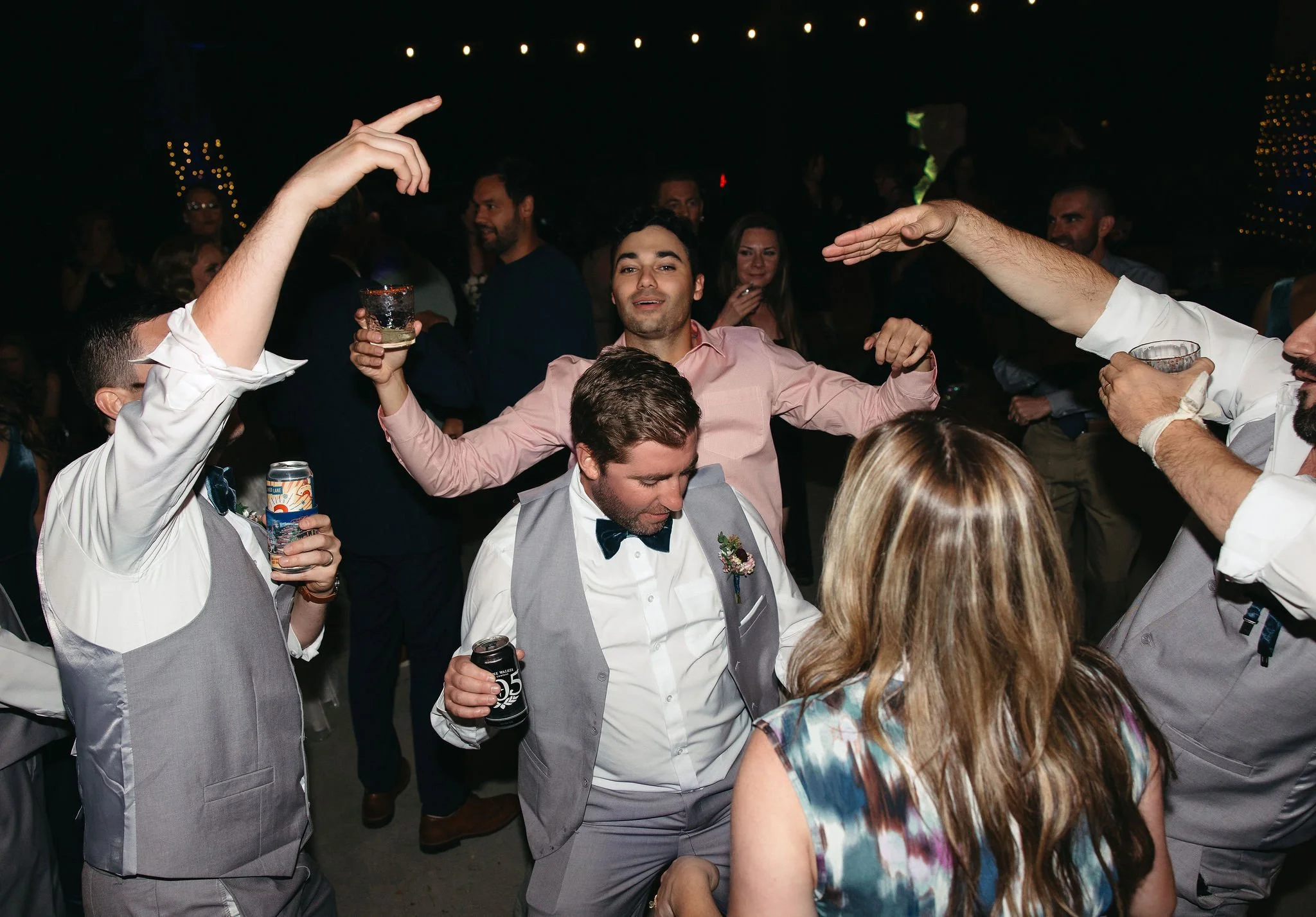 Group of people dancing and celebrating at a party, with some holding drinks and others raising their hands