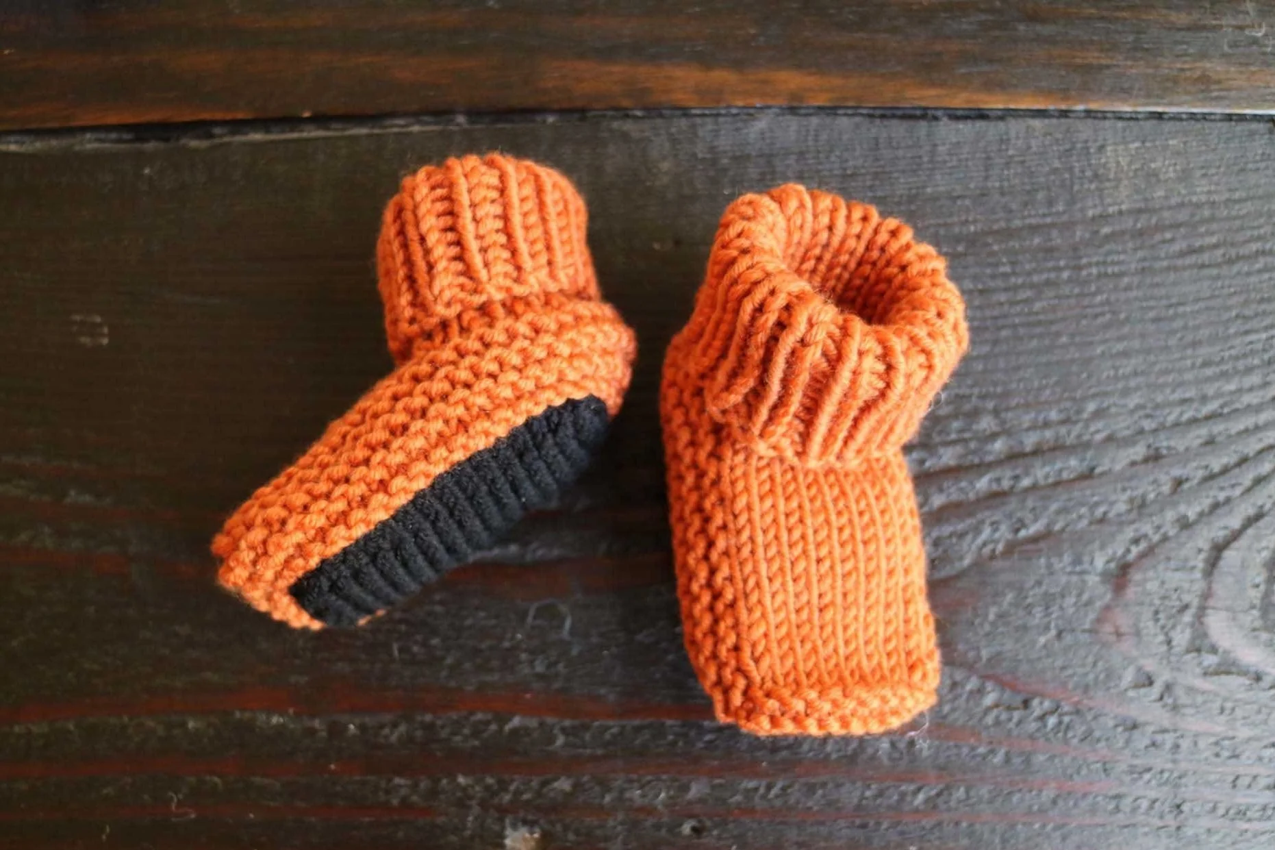 This image shows an orange and black pair of baby socks. The sole is black and the rest of the sock is orange. Great gift to knit for a newborn.