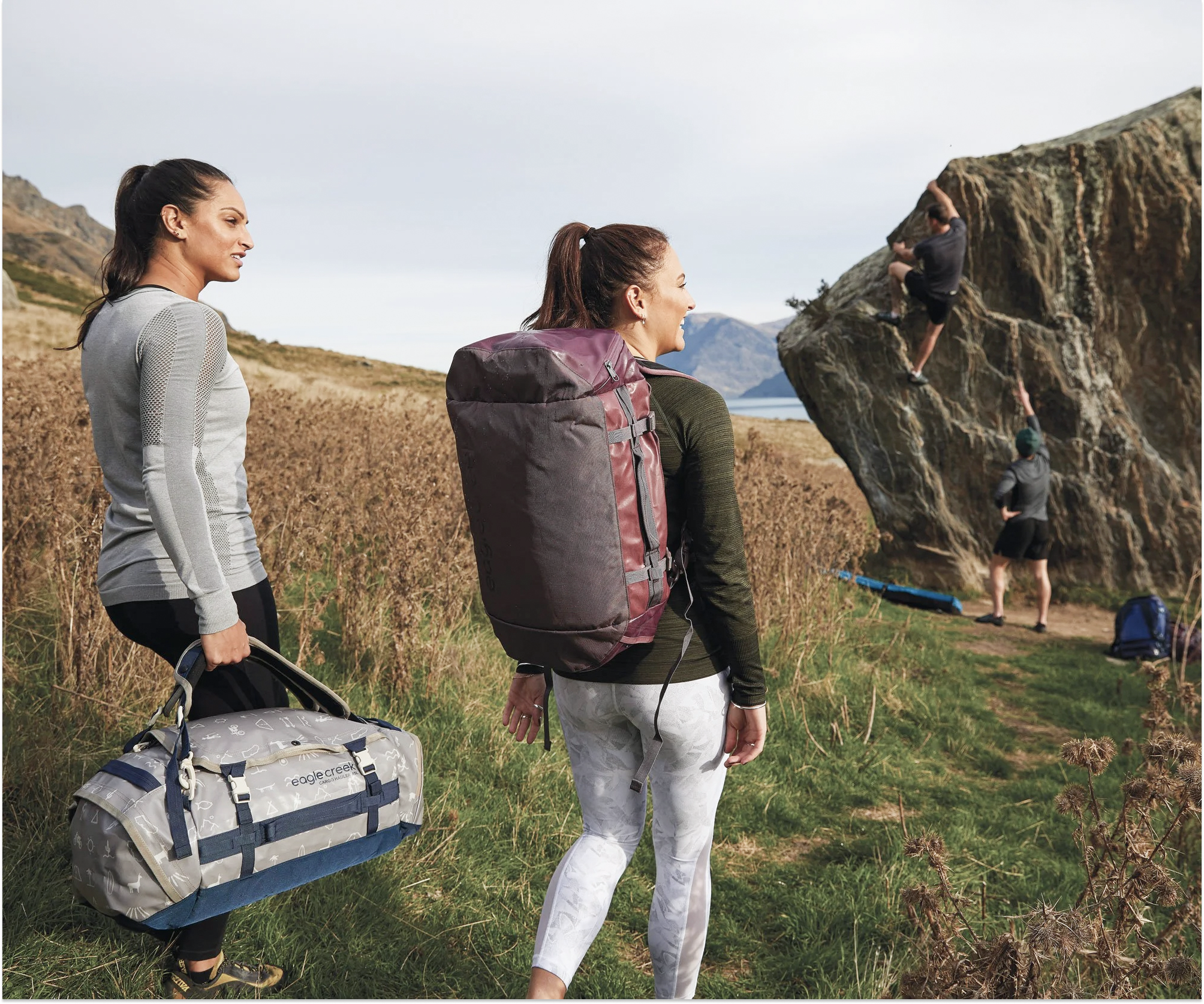 Two women hiking toward a mountain climbing challenge, carrying Eagle Creek bags. This image represents teamwork and reflects our shared values of curiosity and exploration.
