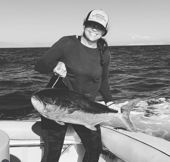 A black and white photo of Danica Carey, Director of Marketing Operations at Seirus Innovation, smiling on a boat while holding a large fish she caught.