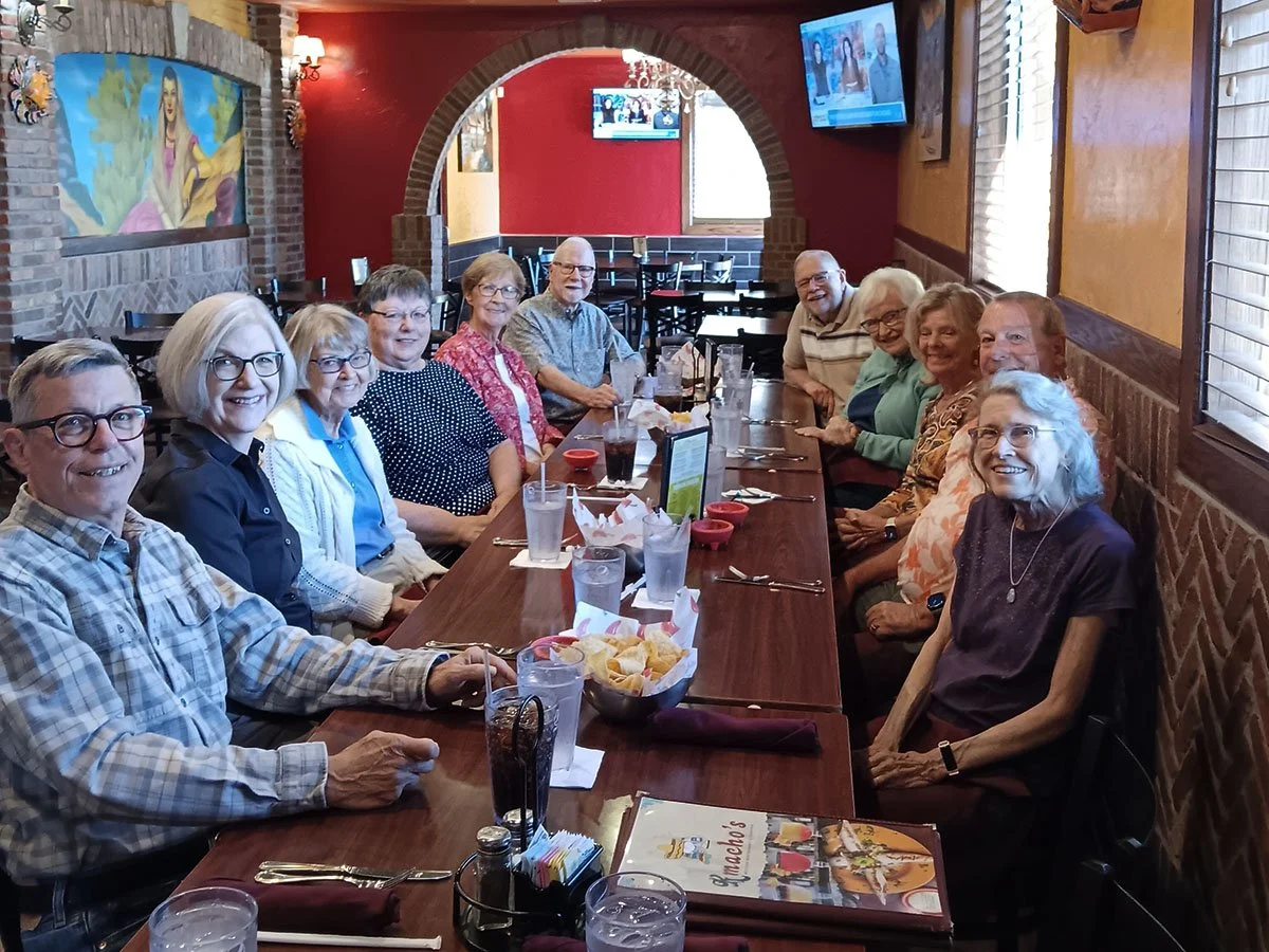 A group of elderly people sitting around a long wooden table at a restaurant, smiling and enjoying a meal together.