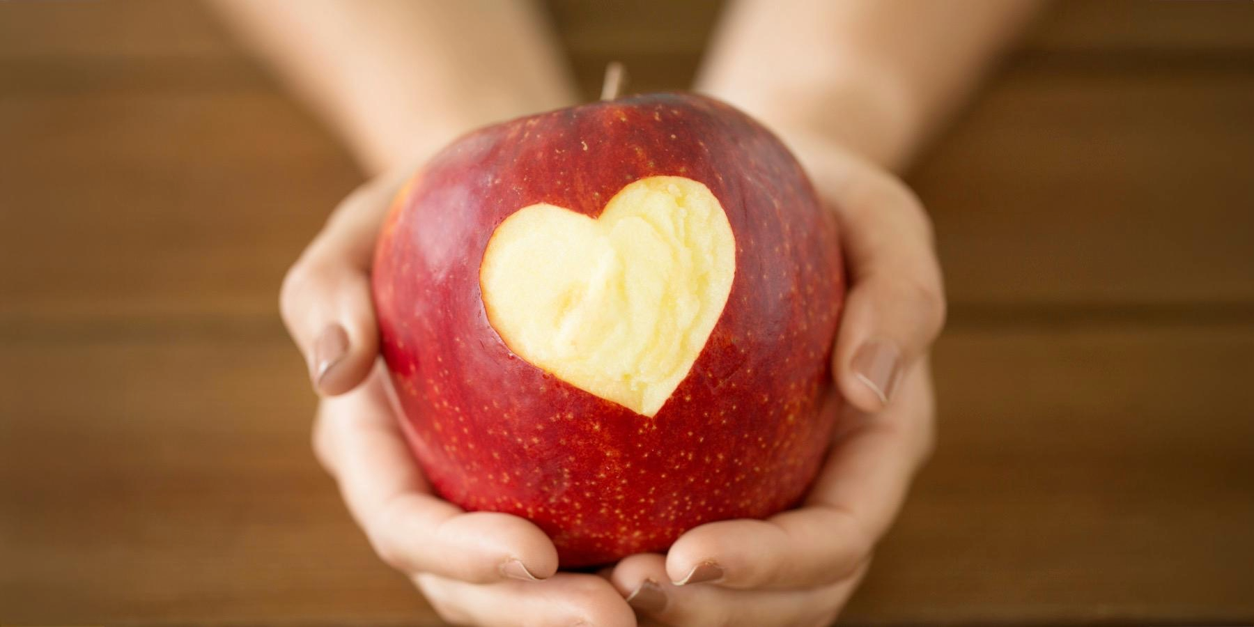 A person holding a red apple with a heart-shaped wedge cut out, showing the white flesh inside.