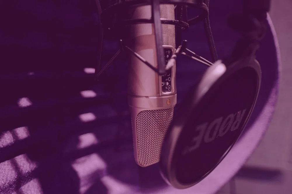 Close-up of a vintage microphone and a Rode headset on a purple surface with shadows.