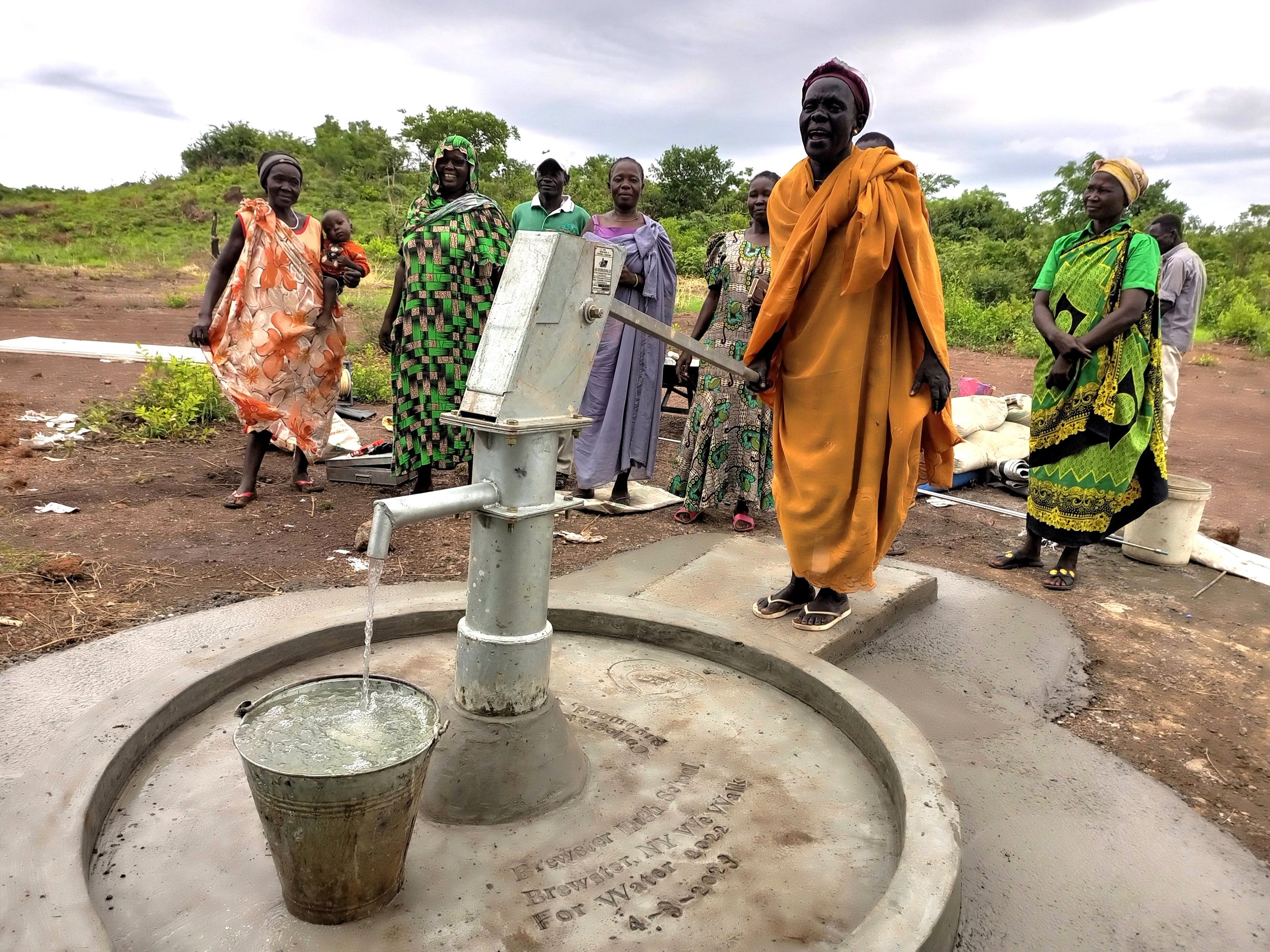 A group of people standing around a newly installed water well in a rural area, with some filling buckets with water.