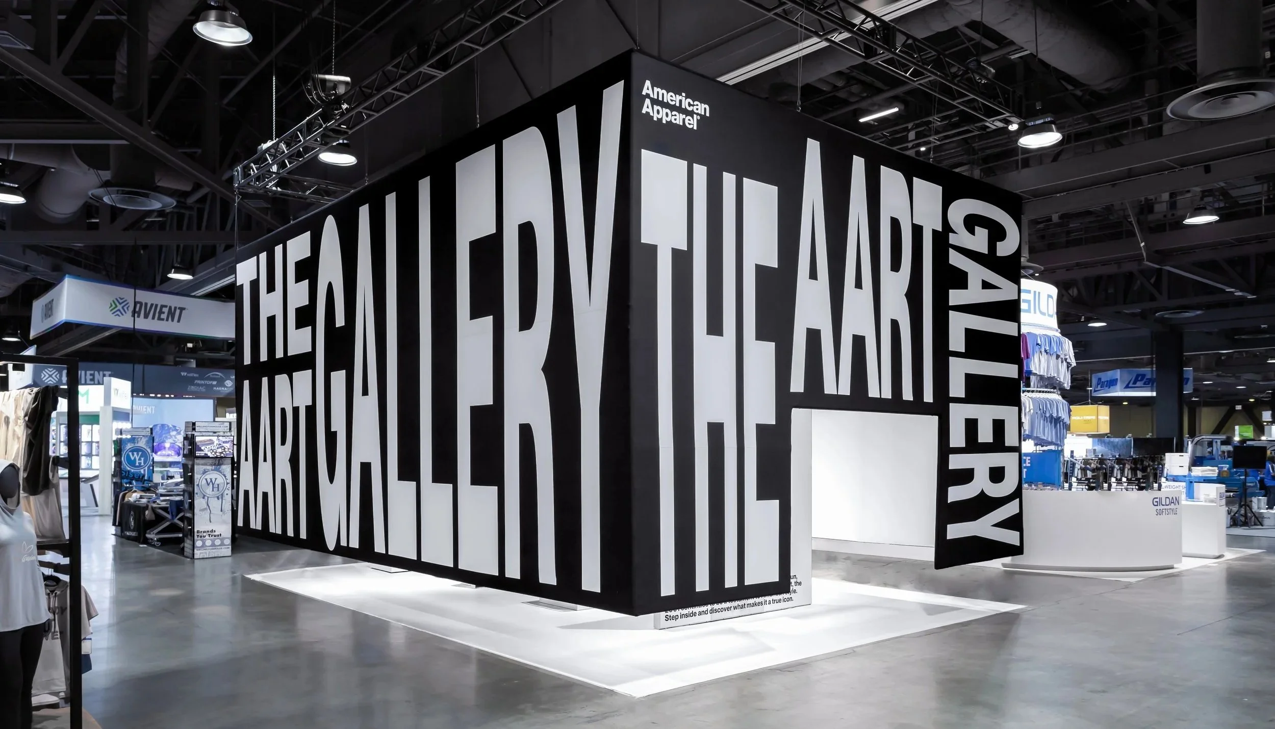 An indoor retail space featuring a large black and white sign with the text "THE GALLERY FROM THE LAST 30 YEARS". The sign is part of an exhibit or store display for American Apparel, surrounded by clothing racks and other retail signage.
