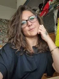 Woman with glasses and wavy hair sitting indoors