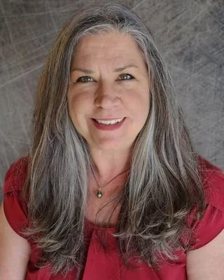 Smiling woman with long gray hair wearing a red top against a textured background