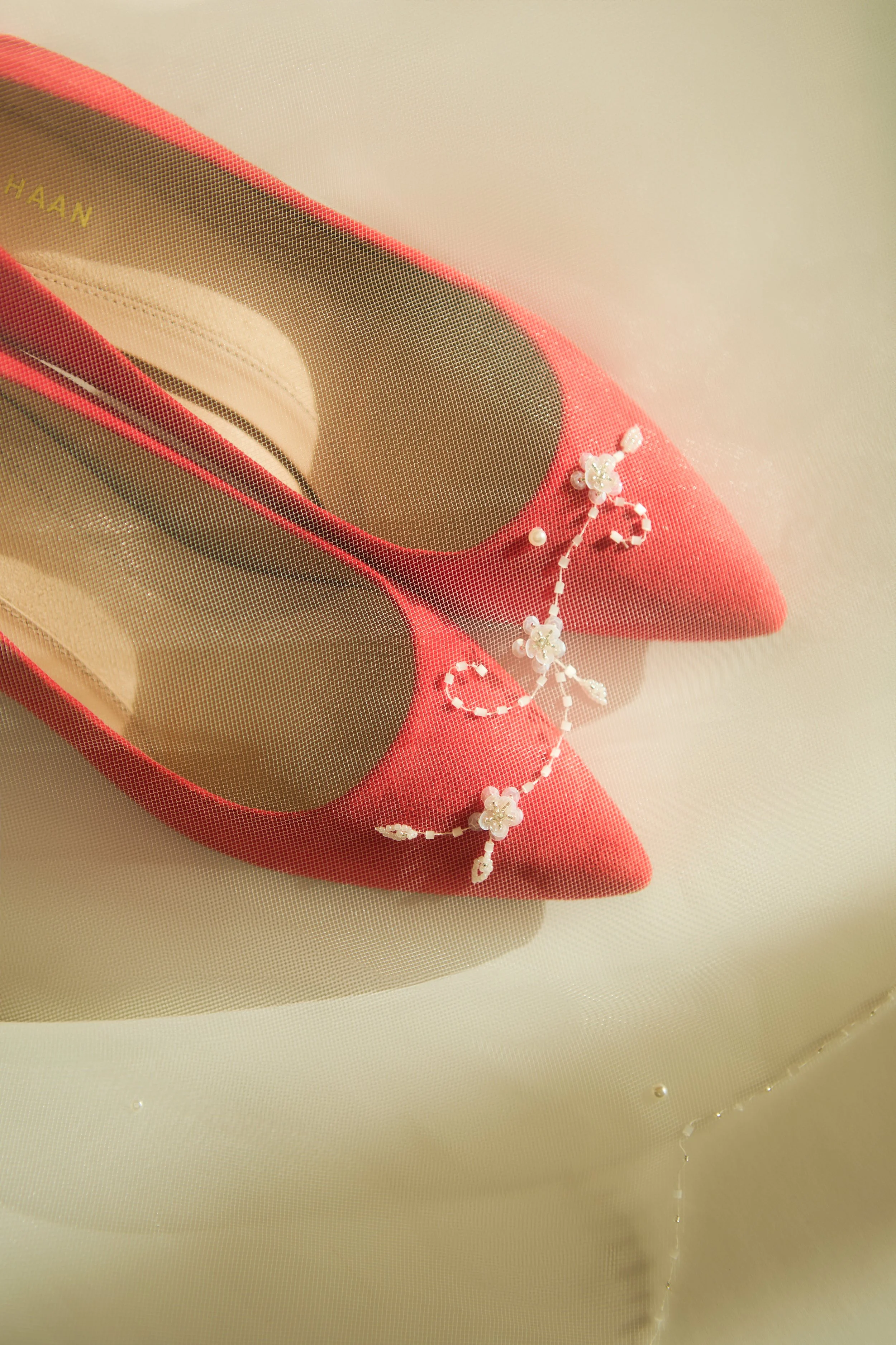 A pair of red high-heeled shoes with a floral headpiece resting on them, viewed through a mesh fabric.