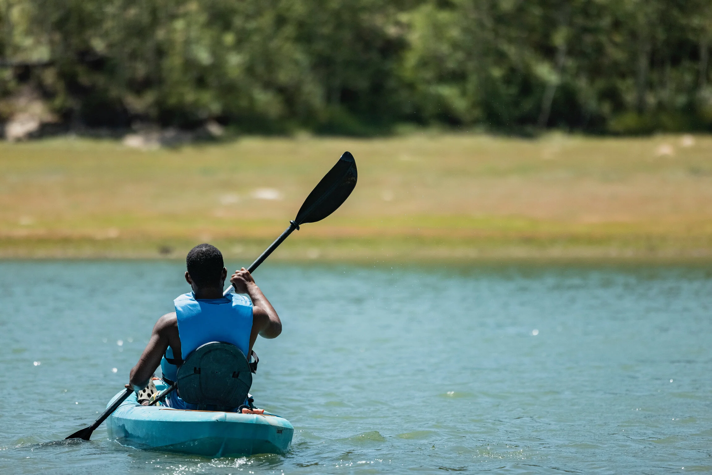 A person kayaking on a body of water with trees in the background.