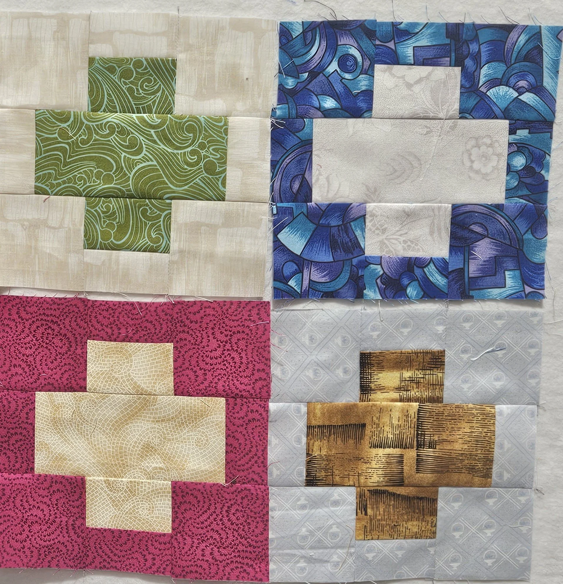 Four squares of bright colours (blue, green, red and yellow) surrounded by a mostly black fabric with white accents, and mostly white fabric with black accents, that are cut diagonally