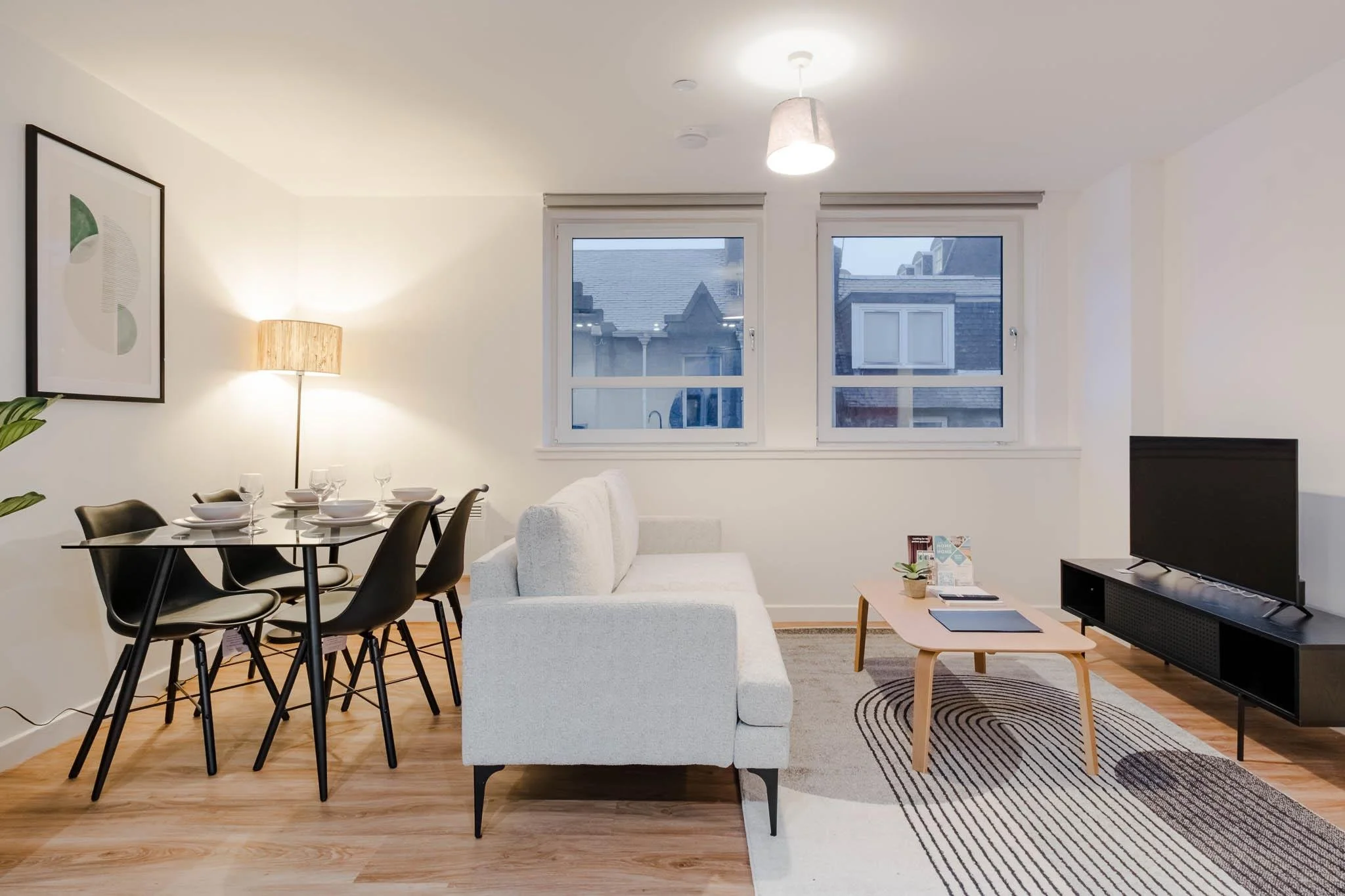 Living room with dining area, white sofa, wooden coffee table, TV on black stand, large windows, and decorative rug.