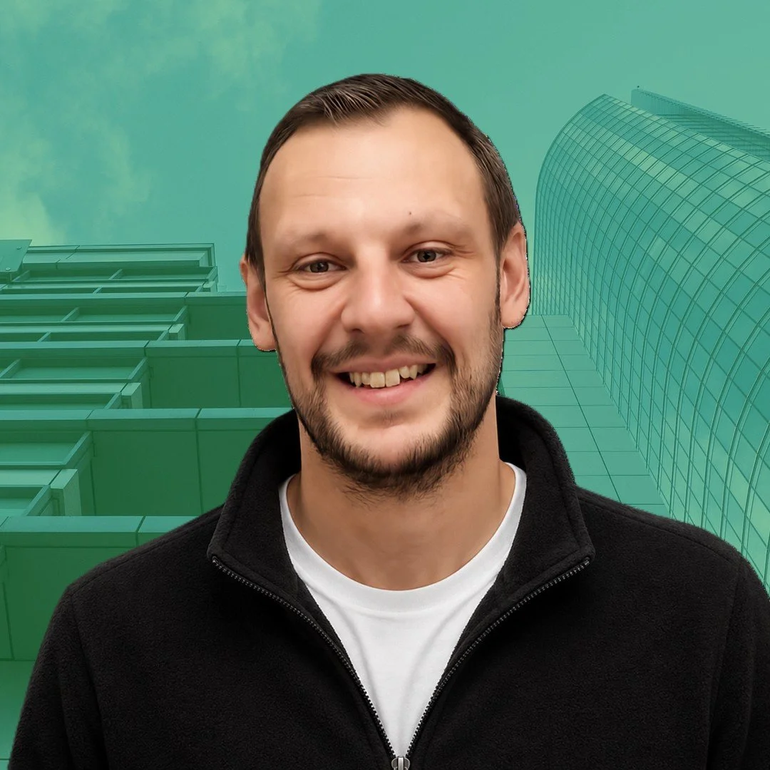 A young man with short brown hair and a beard smiling at the camera, standing in front of digital illustrations of modern office buildings.
