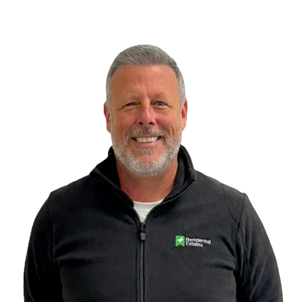 A smiling bald man wearing a black jacket with 'Residential Estates' logo on it.