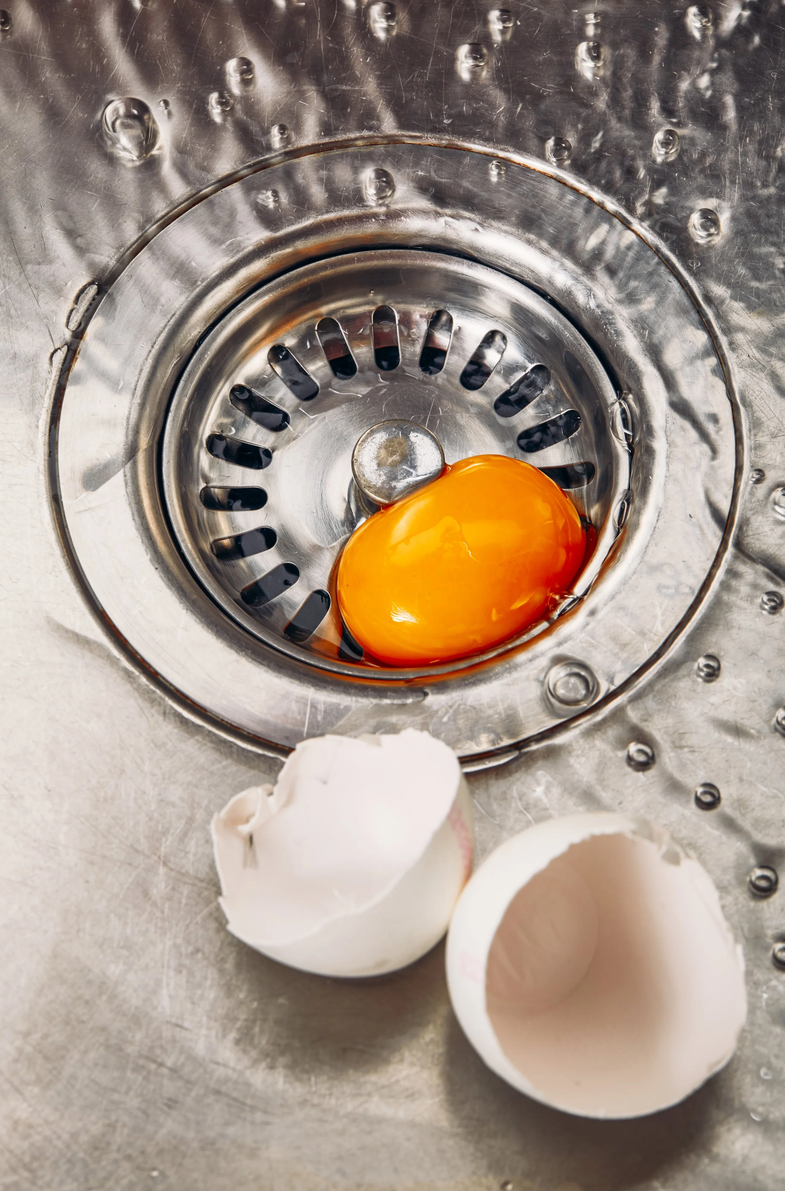 Una yema de huevo en un drenaje de fregadero de cocina junto con cáscaras de huevo.