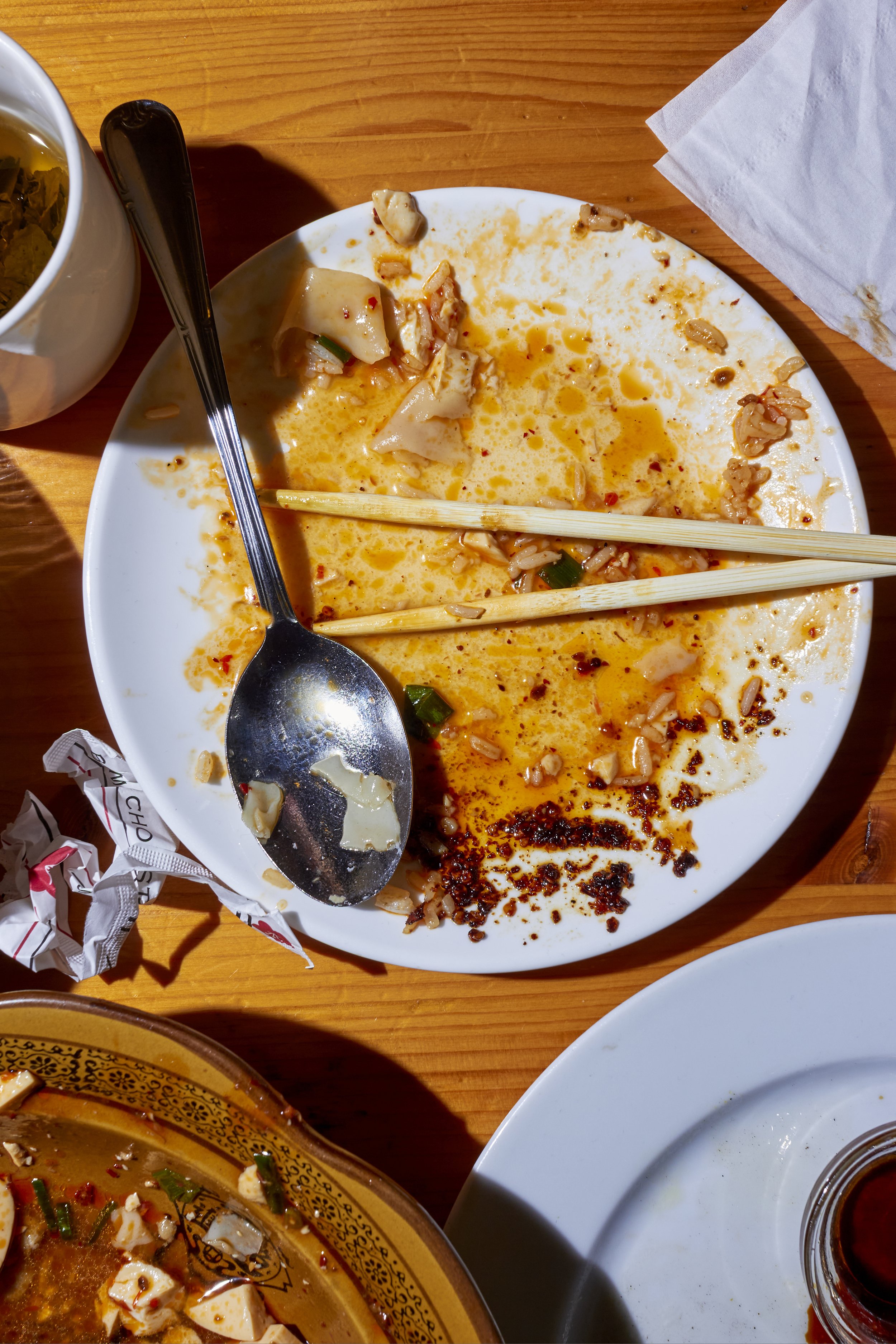 Plato vacío con restos de comida de ramen, con palillos y cuchara en un plato blanco sobre una mesa de madera.