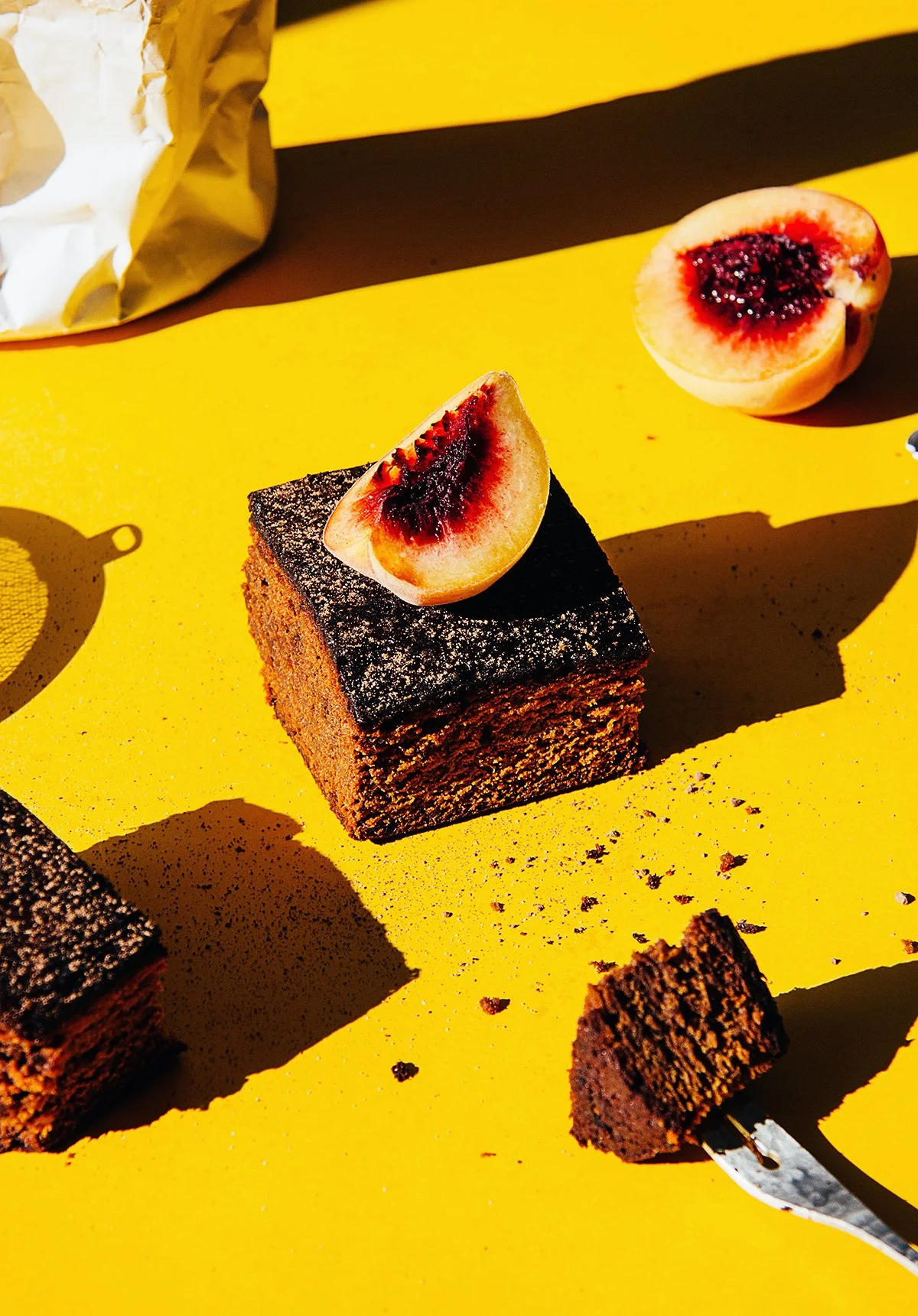 Brownie con un trozo de melocotón encima, sobre un fondo amarillo. Hay medio melocotón a un lado y un bocado de pastel en un tenedor.