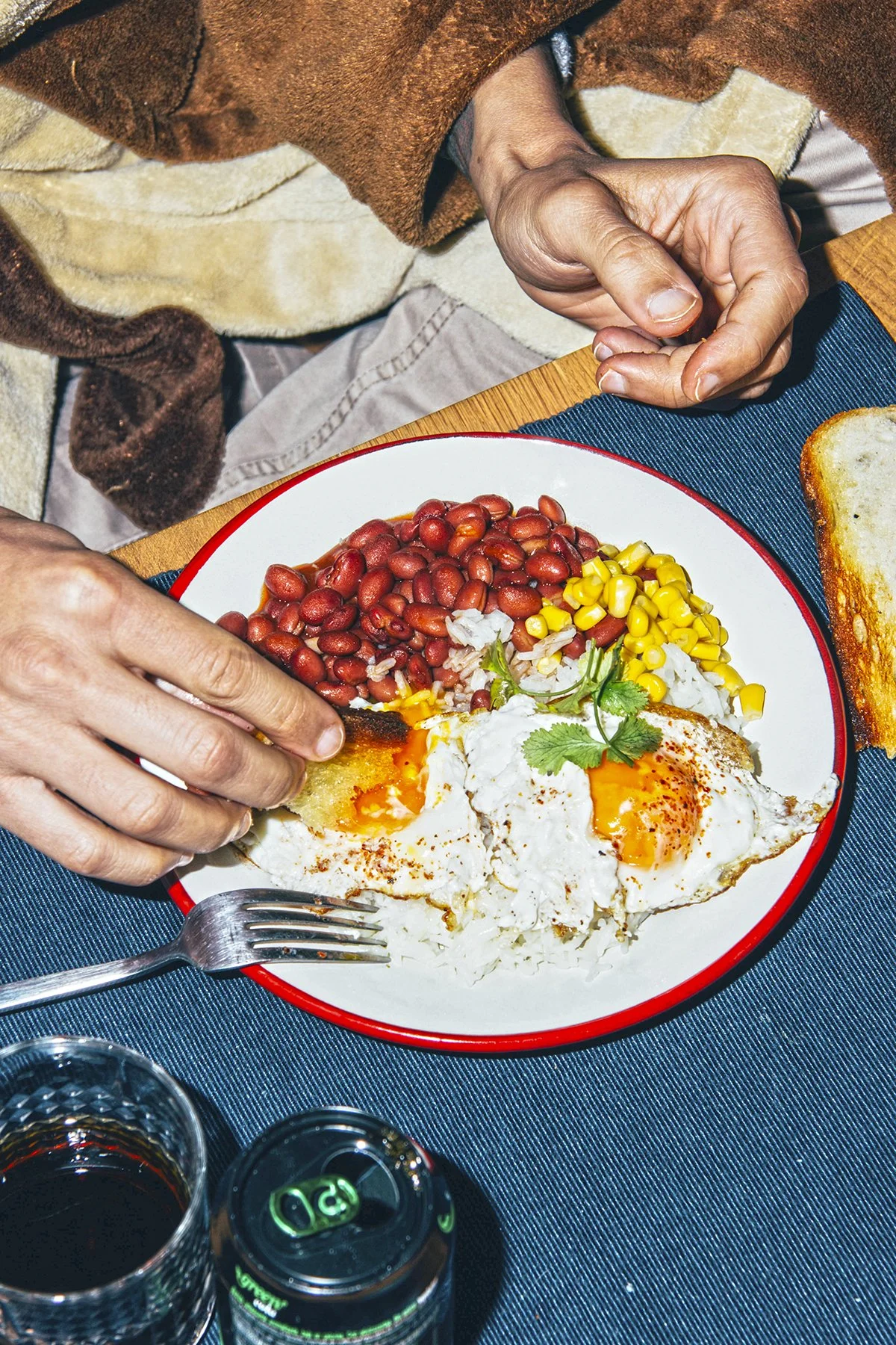 Plato de desayuno latino con arroz, frijoles rojos, maíz, y huevos cocidos con cilantro, acompañado de pan tostado y bebidas.