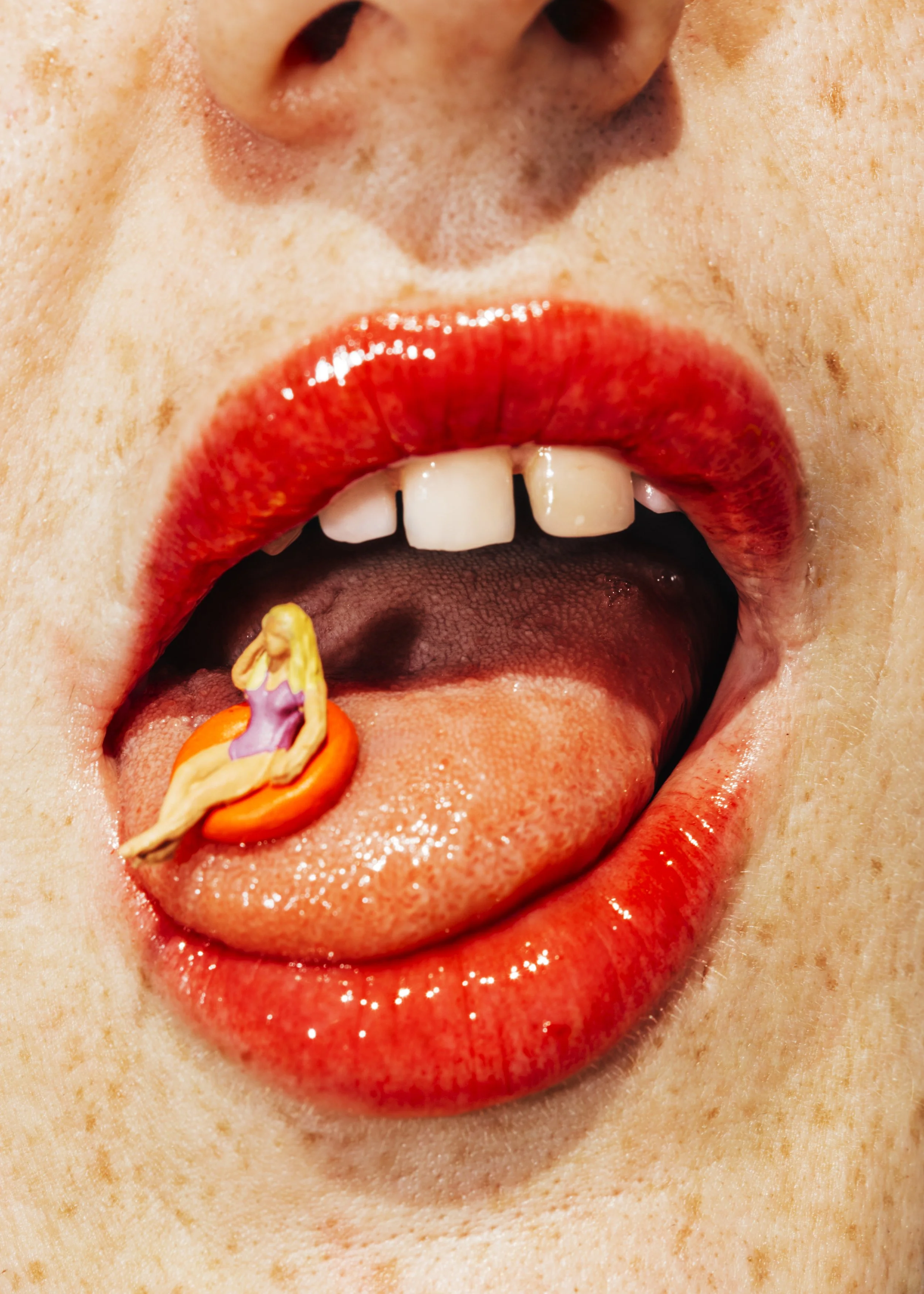 Boca abierta con labios rojos y dientes visibles, lengua con una figura de una mujer en ella.