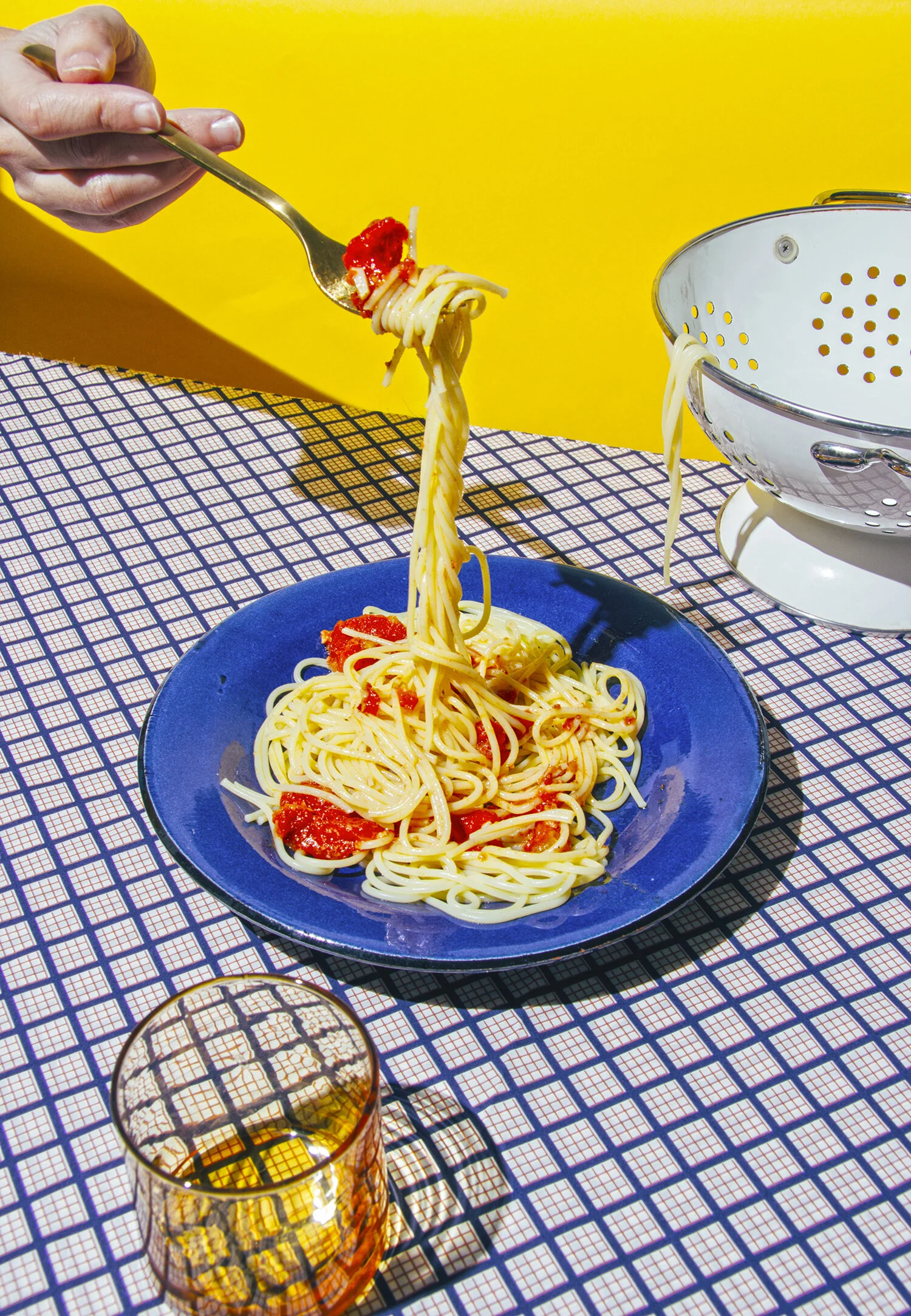 Plato de espaguetis con salsa de tomate en una mesa con fondo amarillo y vaso de bebida al frente.