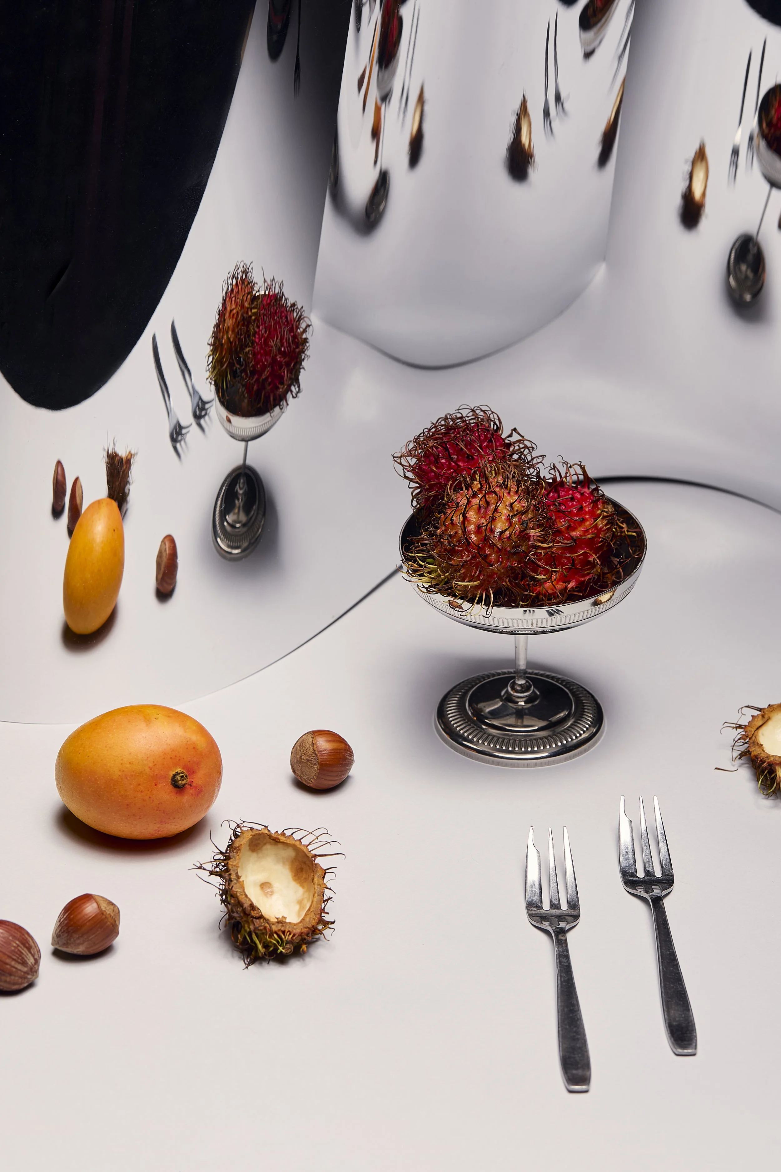 Frutos tropicales, como rambután, mangos y duraznos, con tenedores de plata en una mesa blanca