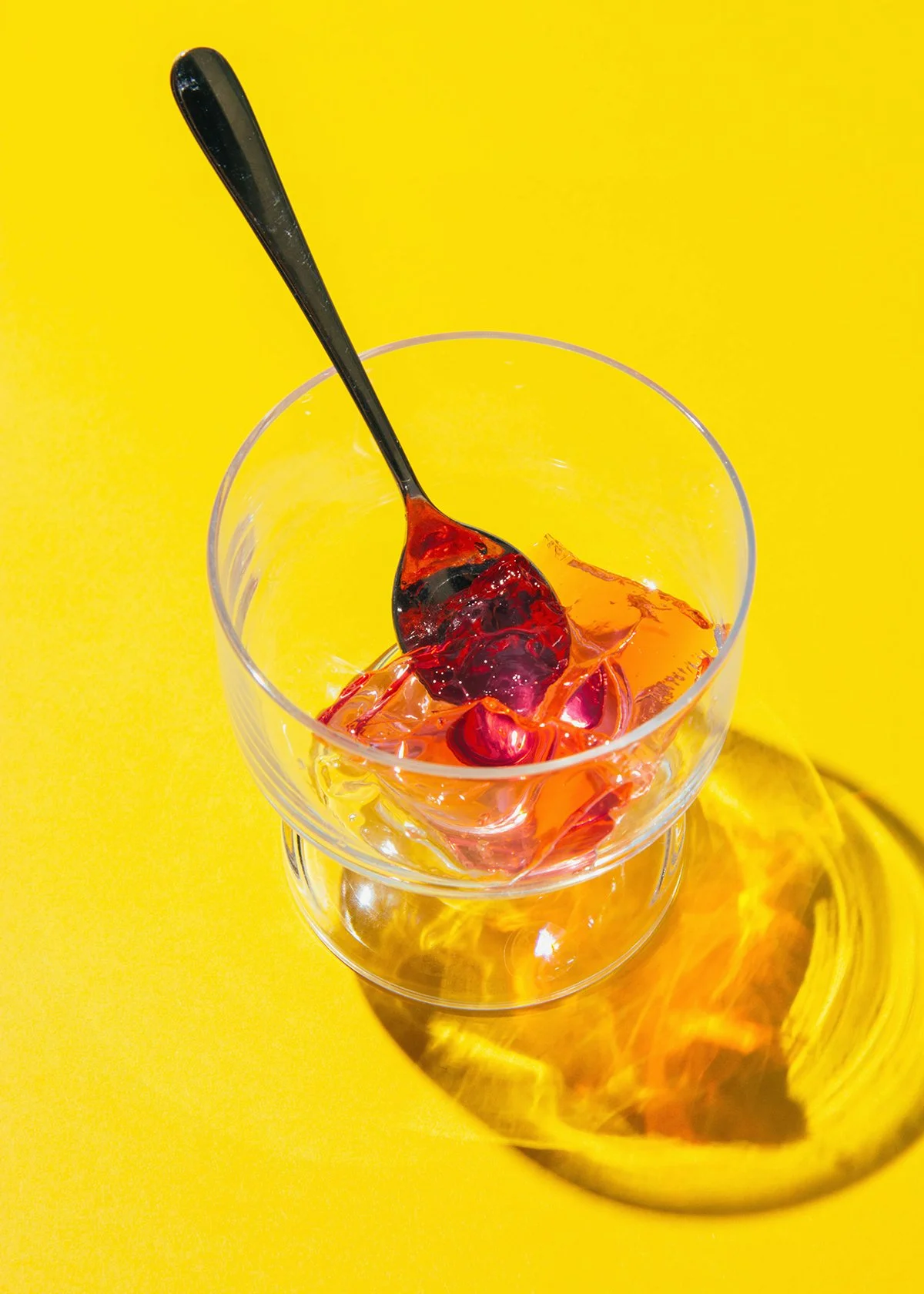 Cucharadita con mermelada de frutas en vaso de cristal sobre fondo amarillo