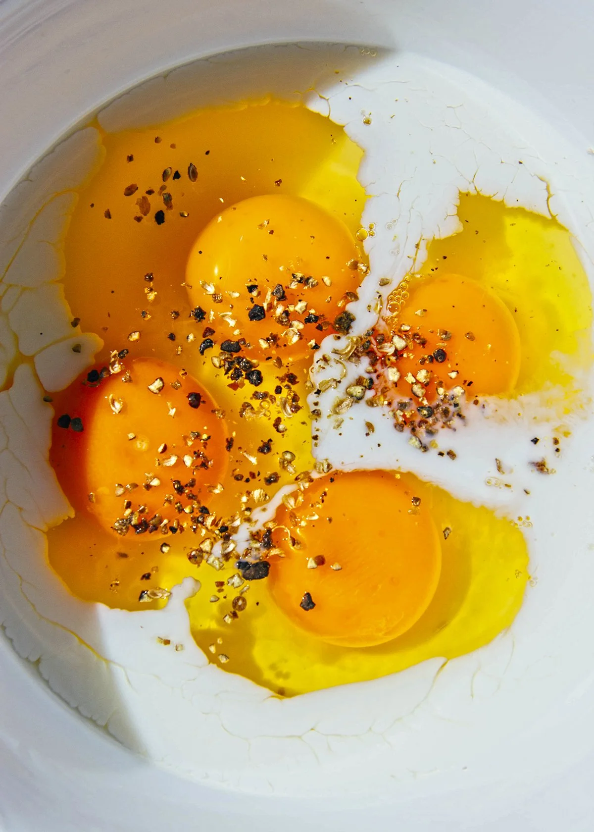 Cinco huevos crudos en un recipiente con sal y pimienta.